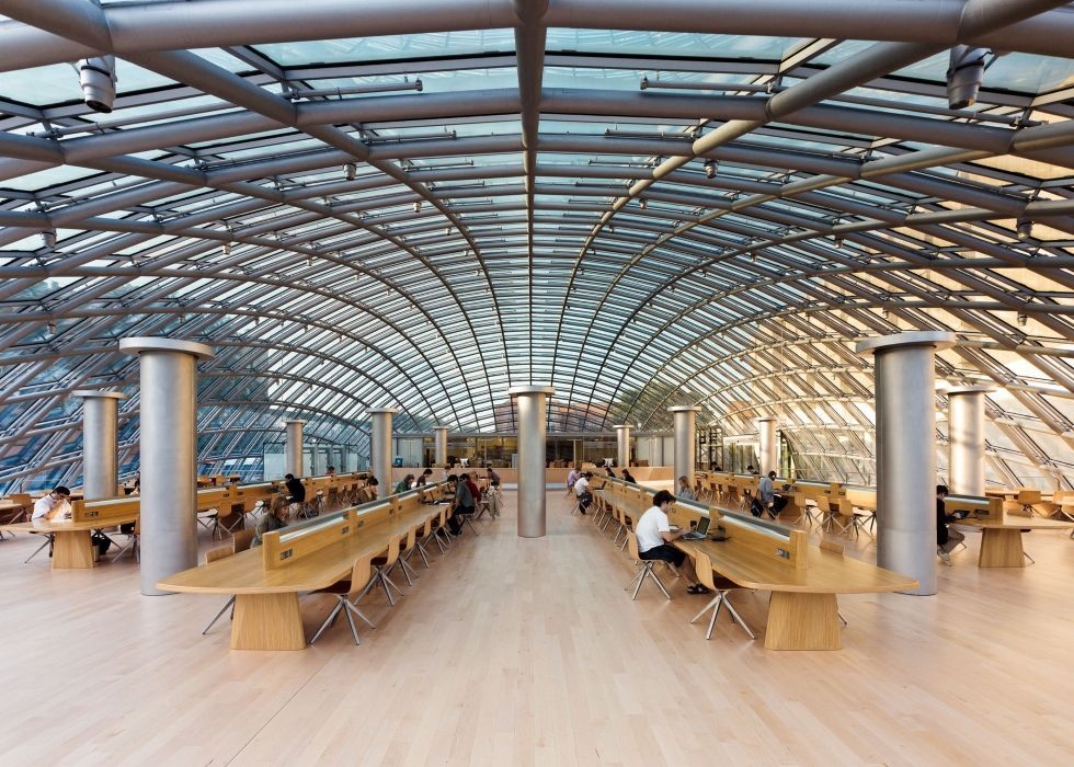 A group of people are sitting at tables in a large room with a glass ceiling.