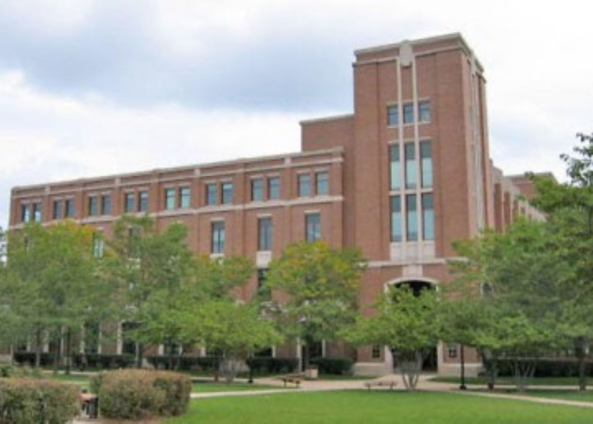 A large brick building is surrounded by trees and grass