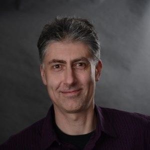 A man in a purple shirt is smiling for the camera.