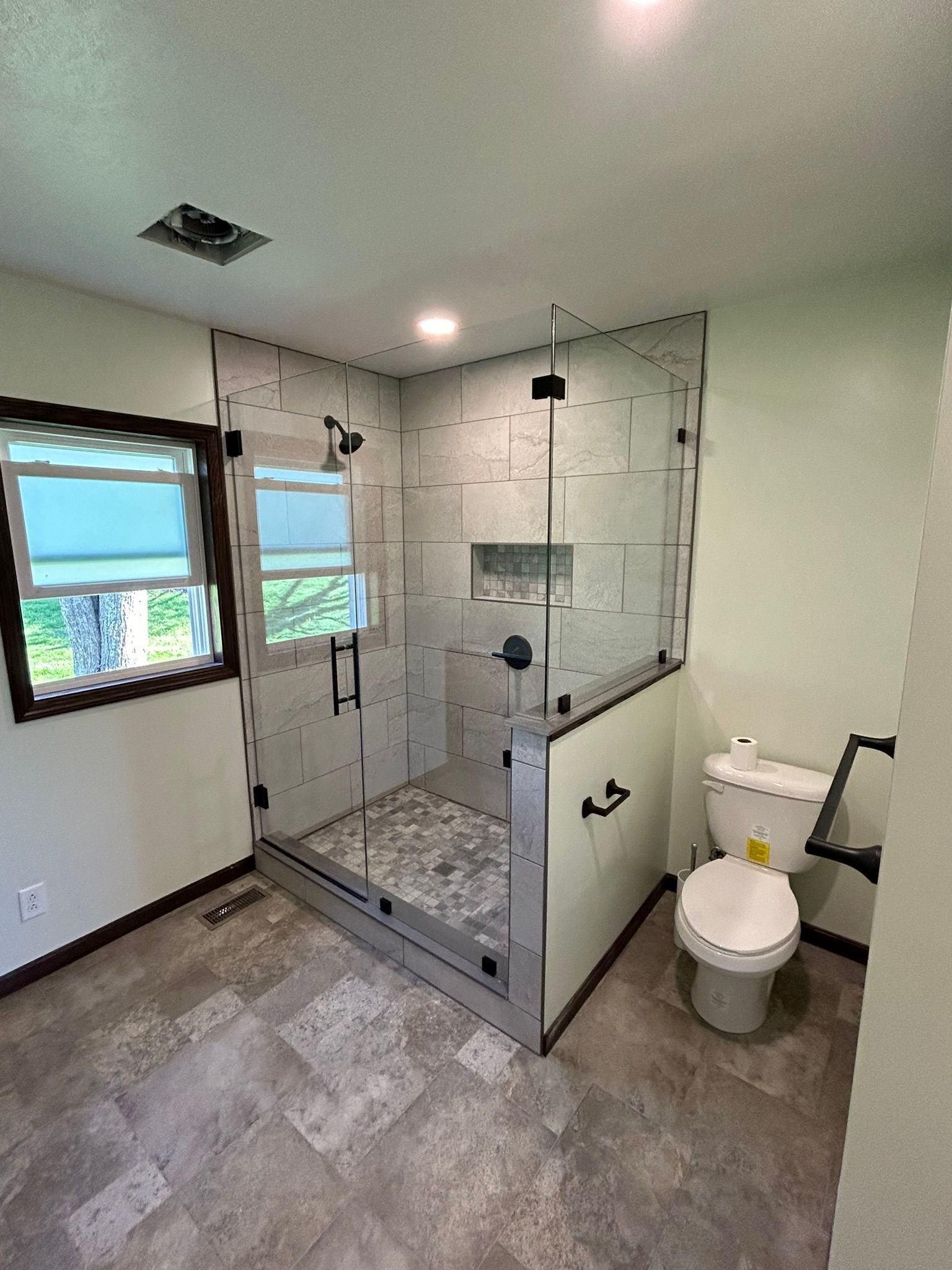 A bathroom with a toilet , shower , and window.