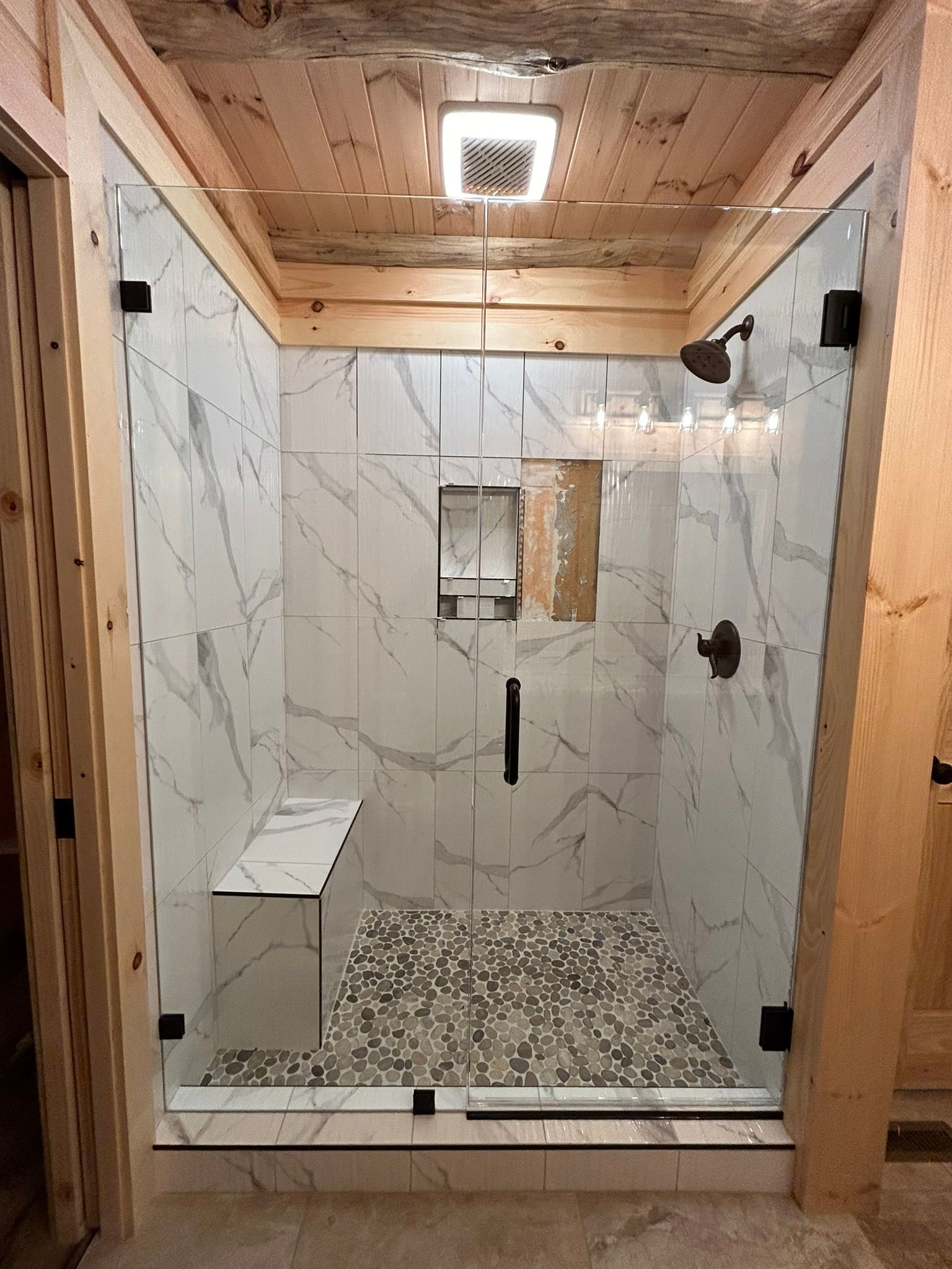A bathroom with a walk in shower with marble tiles and a bench.