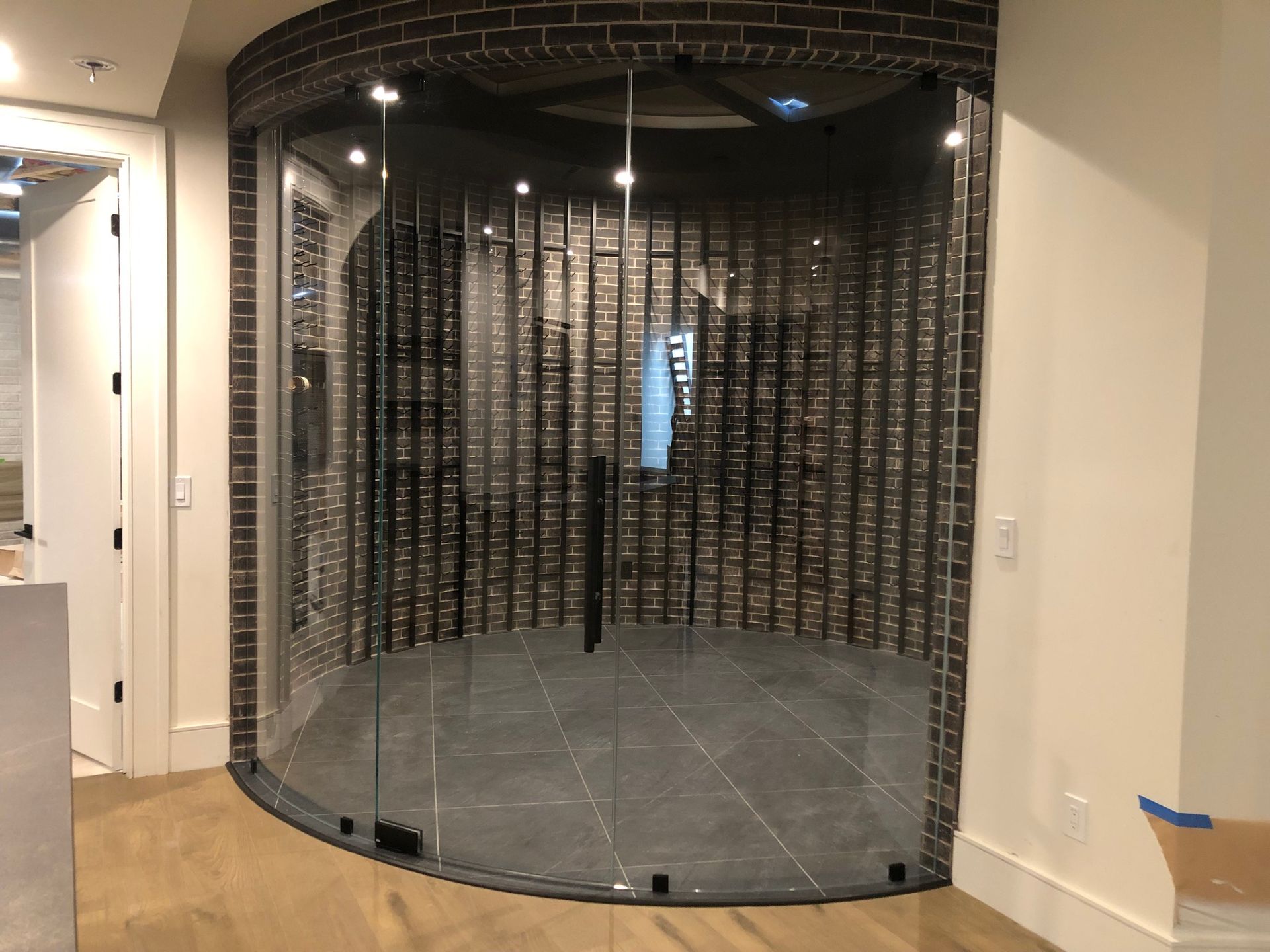 A wine cellar with a curved glass door and a brick wall.