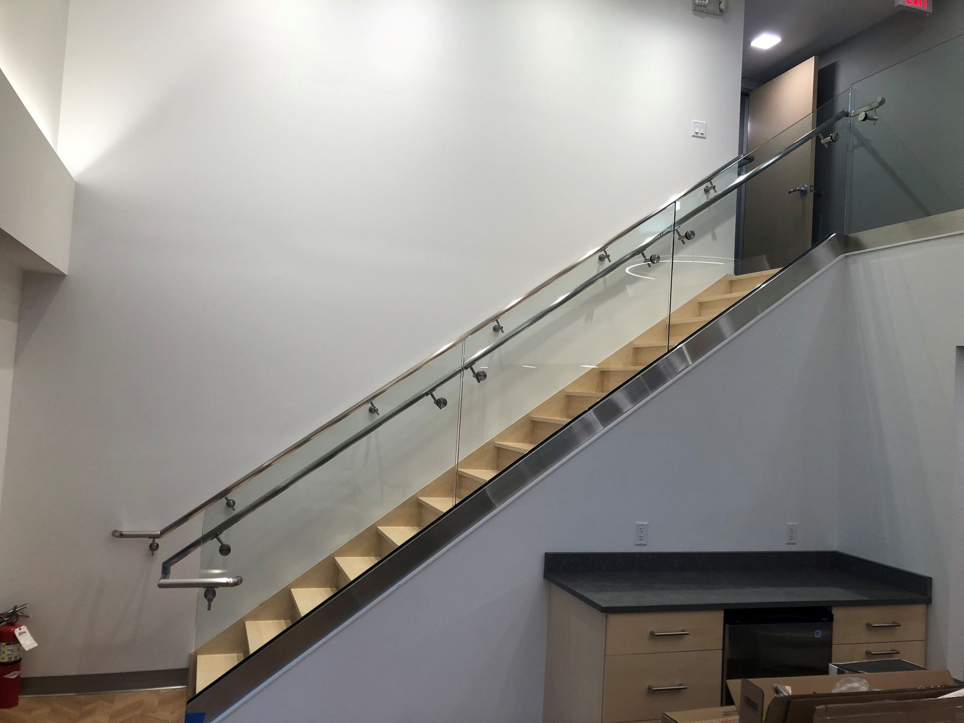 Staircase with glass railing, metal trim, and wooden steps. Grey walls, a built-in counter and cabinets below.