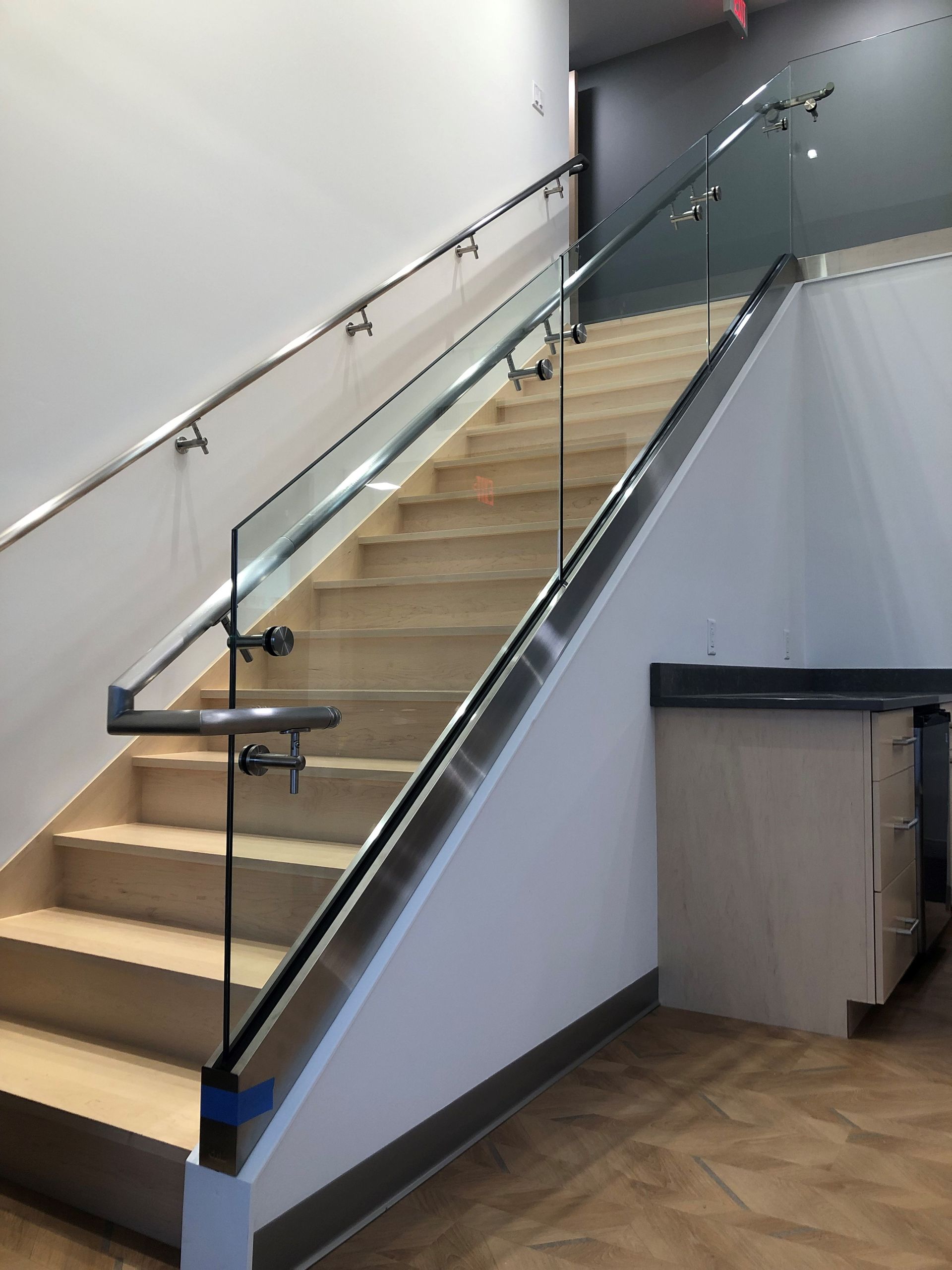 Staircase with glass and metal railing, concrete steps, and white walls.