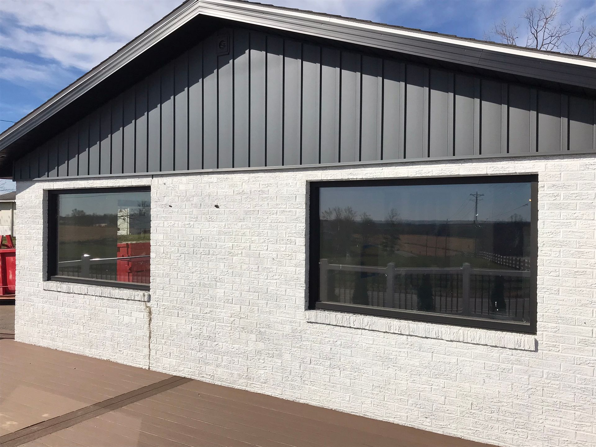 Gray brick building with two windows. Dark gray siding above the windows.