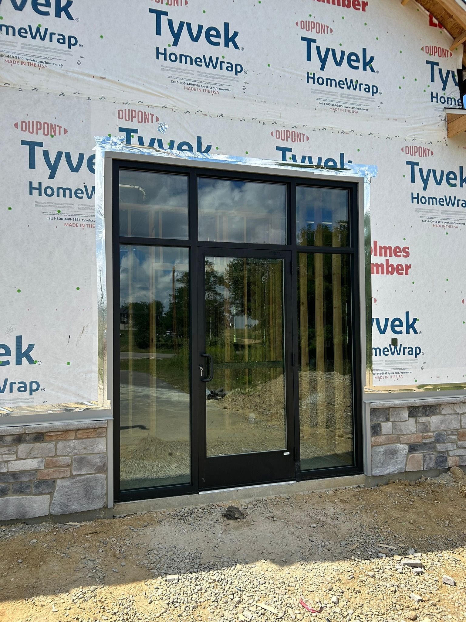 Black framed glass door and side panels on a building under construction, exterior view.