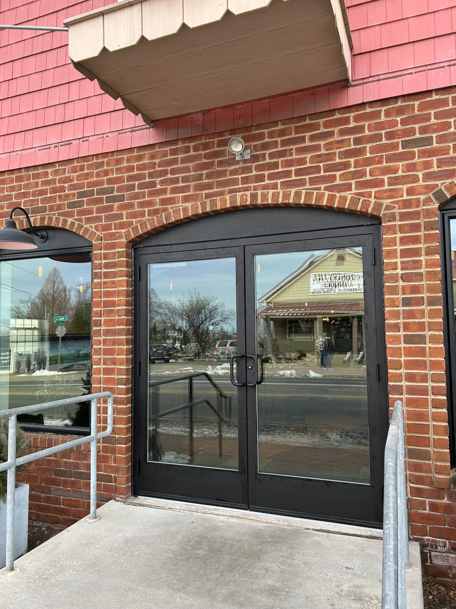 Exterior of a brick building with arched, glass double doors and a ramp. The doors have black frames.