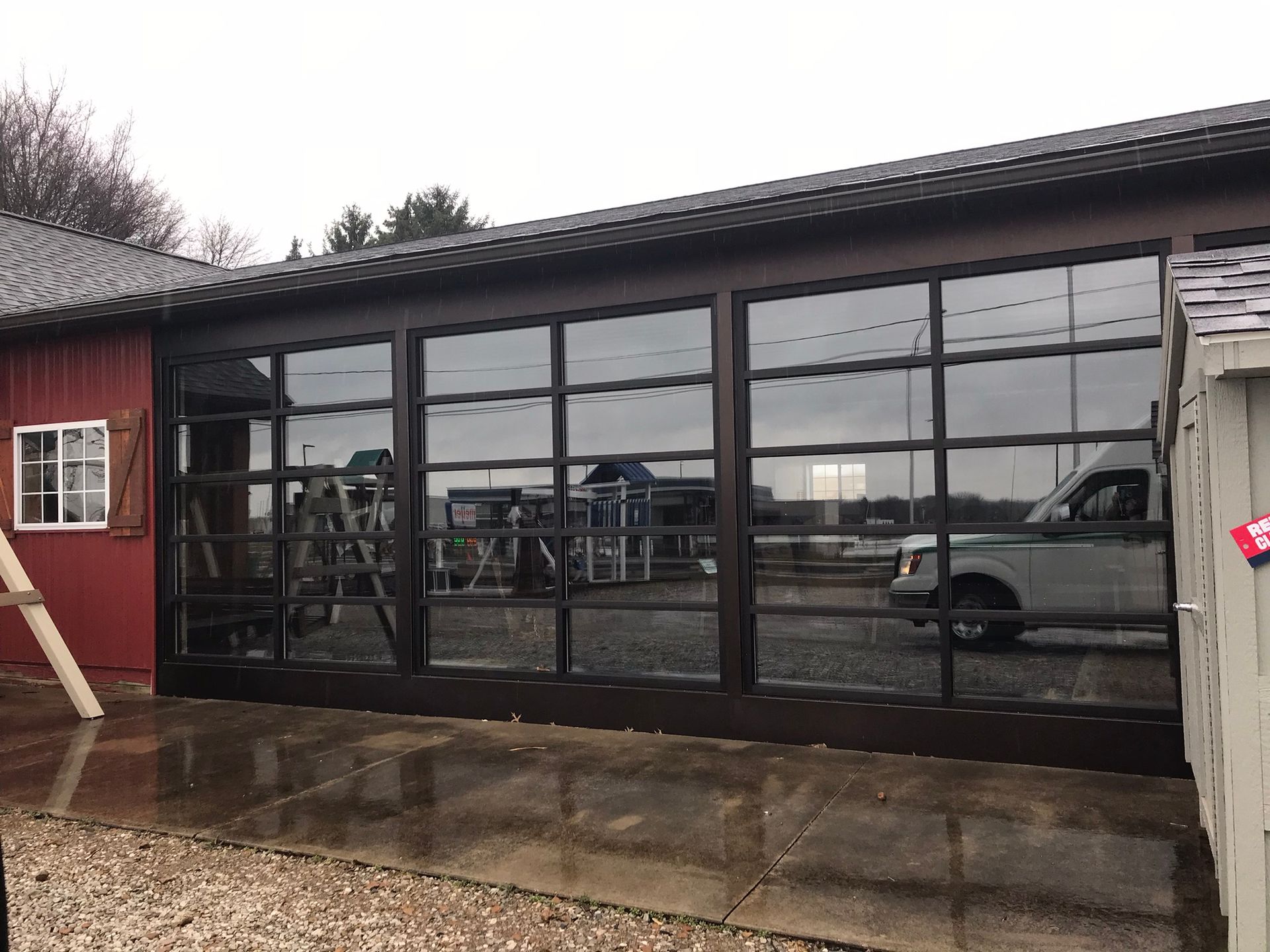 Garage with large glass windows reflecting surroundings, parked vehicles, and building.