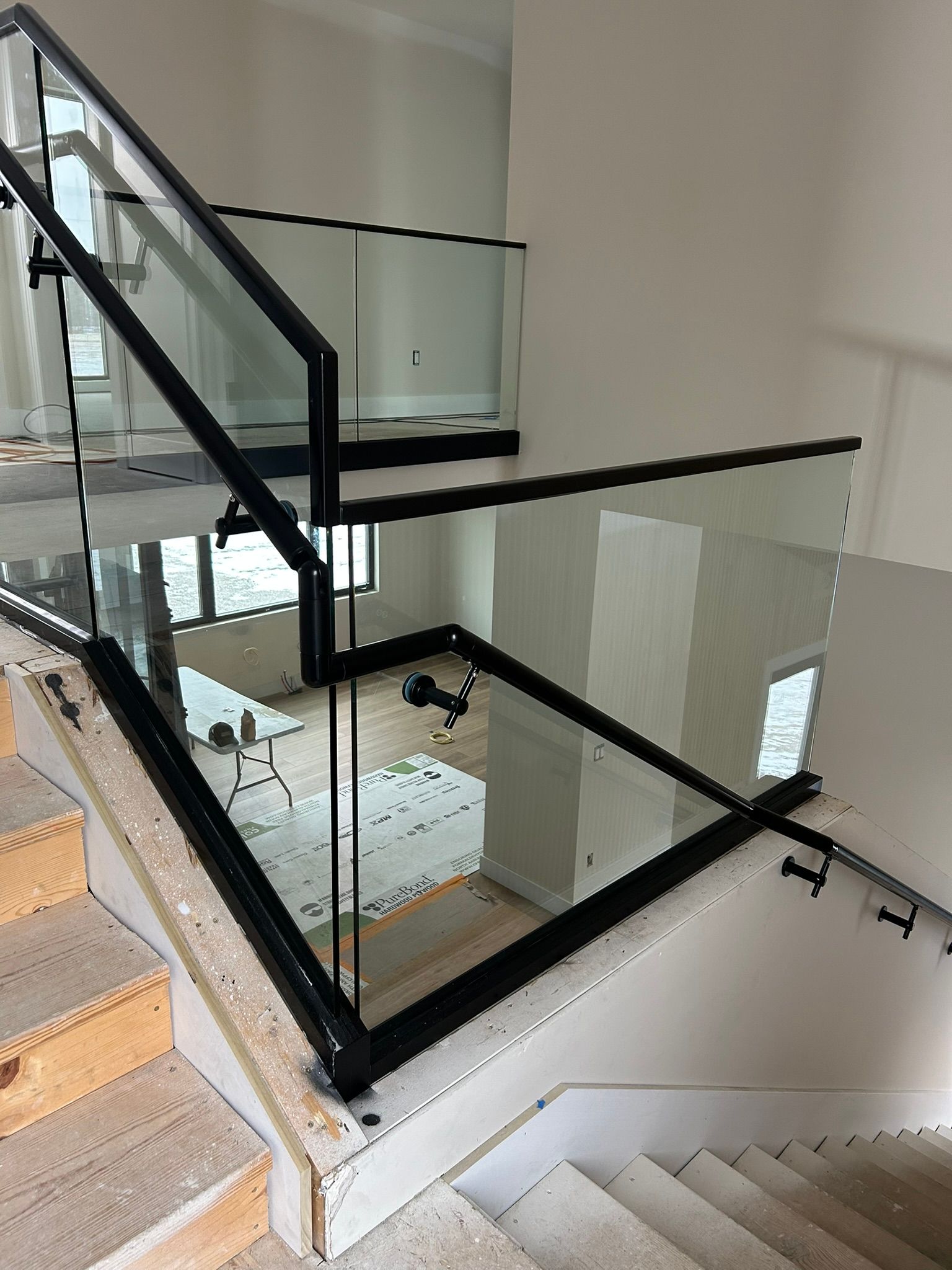 Staircase with black metal and glass railings. Steps are wood. Interior setting, well-lit.