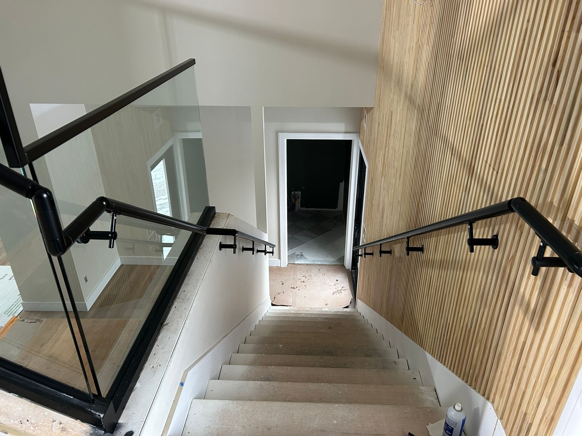 Staircase with black metal handrails and glass panels, leading down. Textured wall on right.