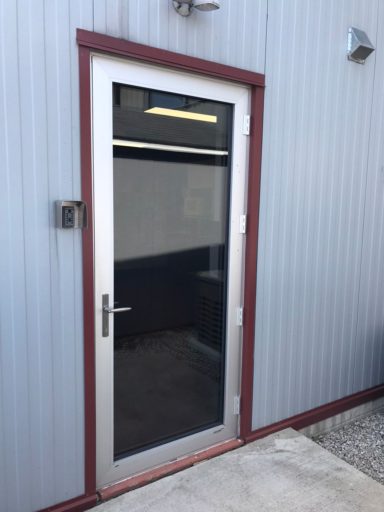 Door with a glass window, surrounded by a metal frame and red trim, on a corrugated metal wall.