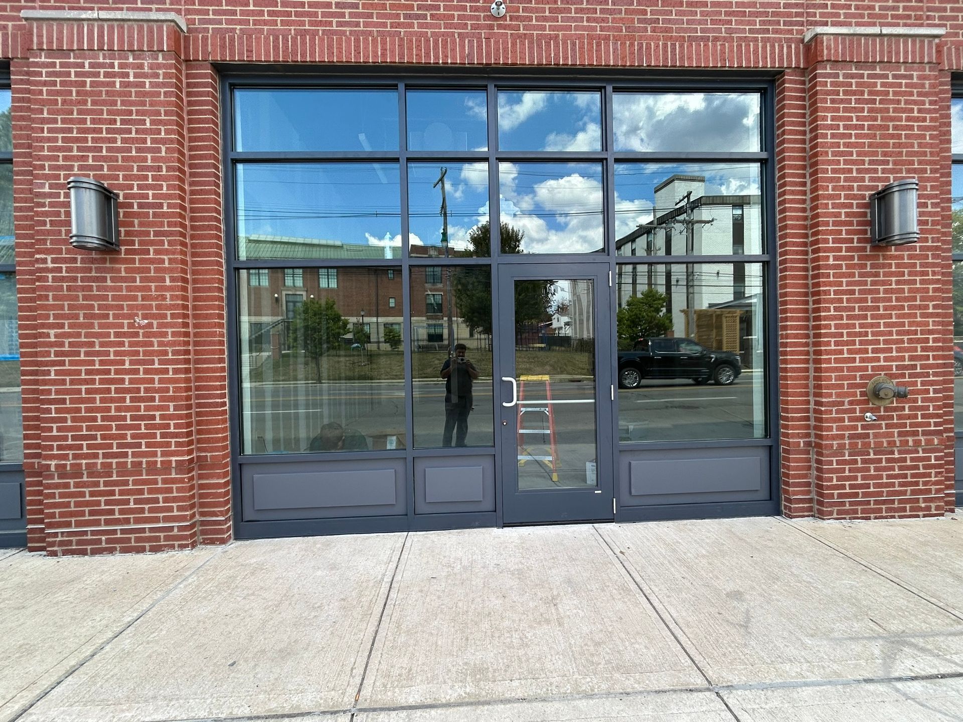 Brick building with large windows reflecting sky and surrounding buildings; entrance door centered.