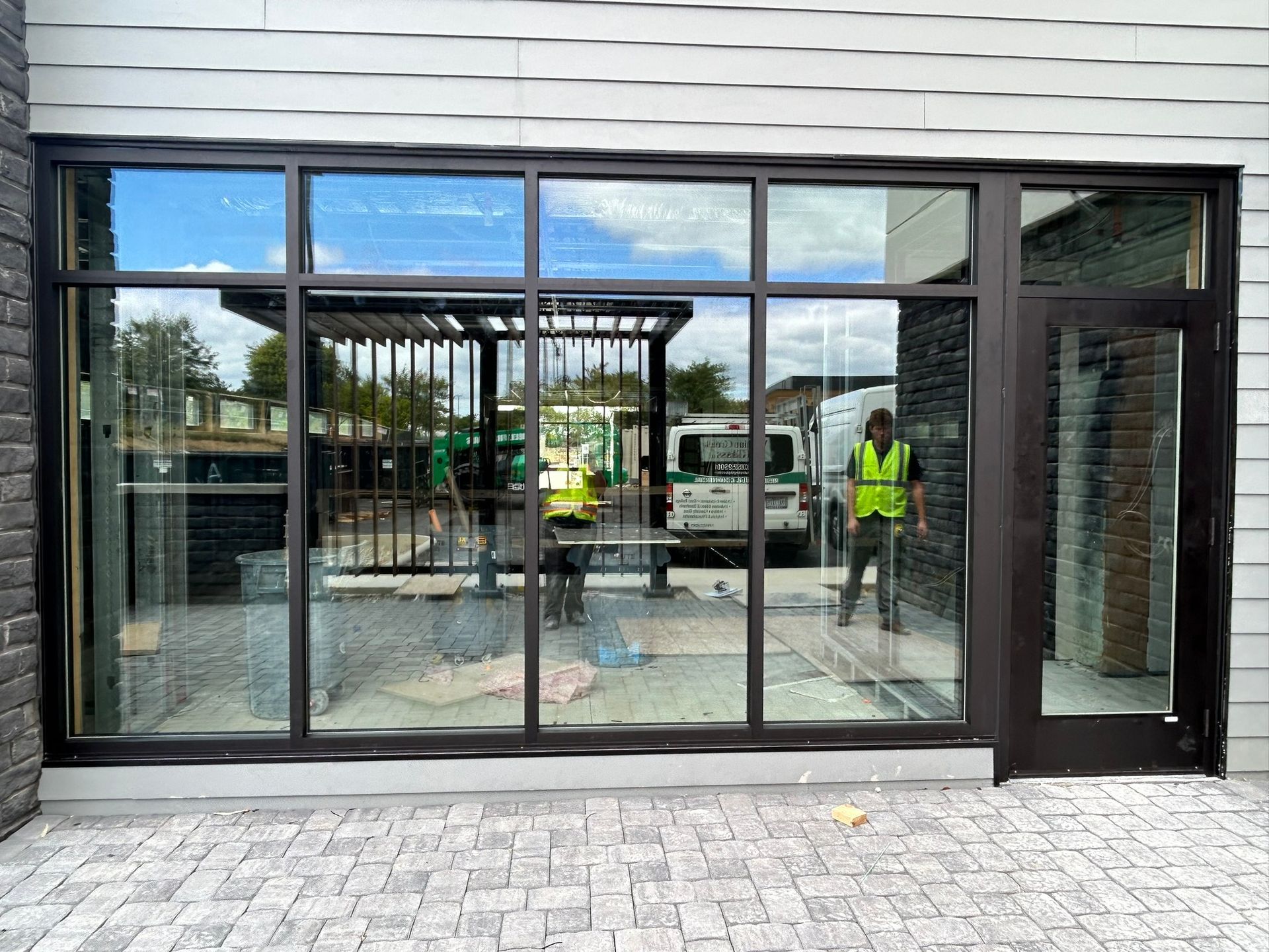Exterior storefront with large windows and a door reflecting a construction scene.