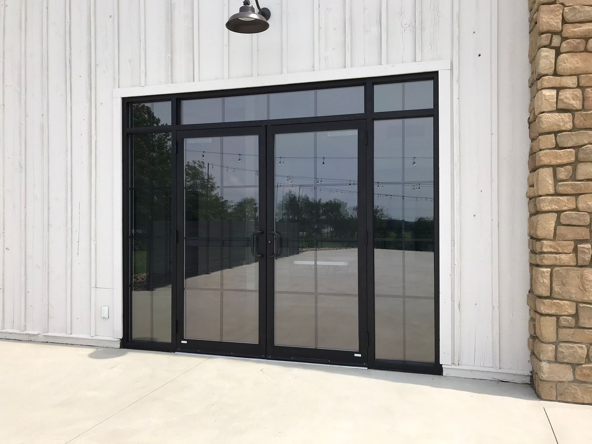Black framed glass doors on white building with stone column.