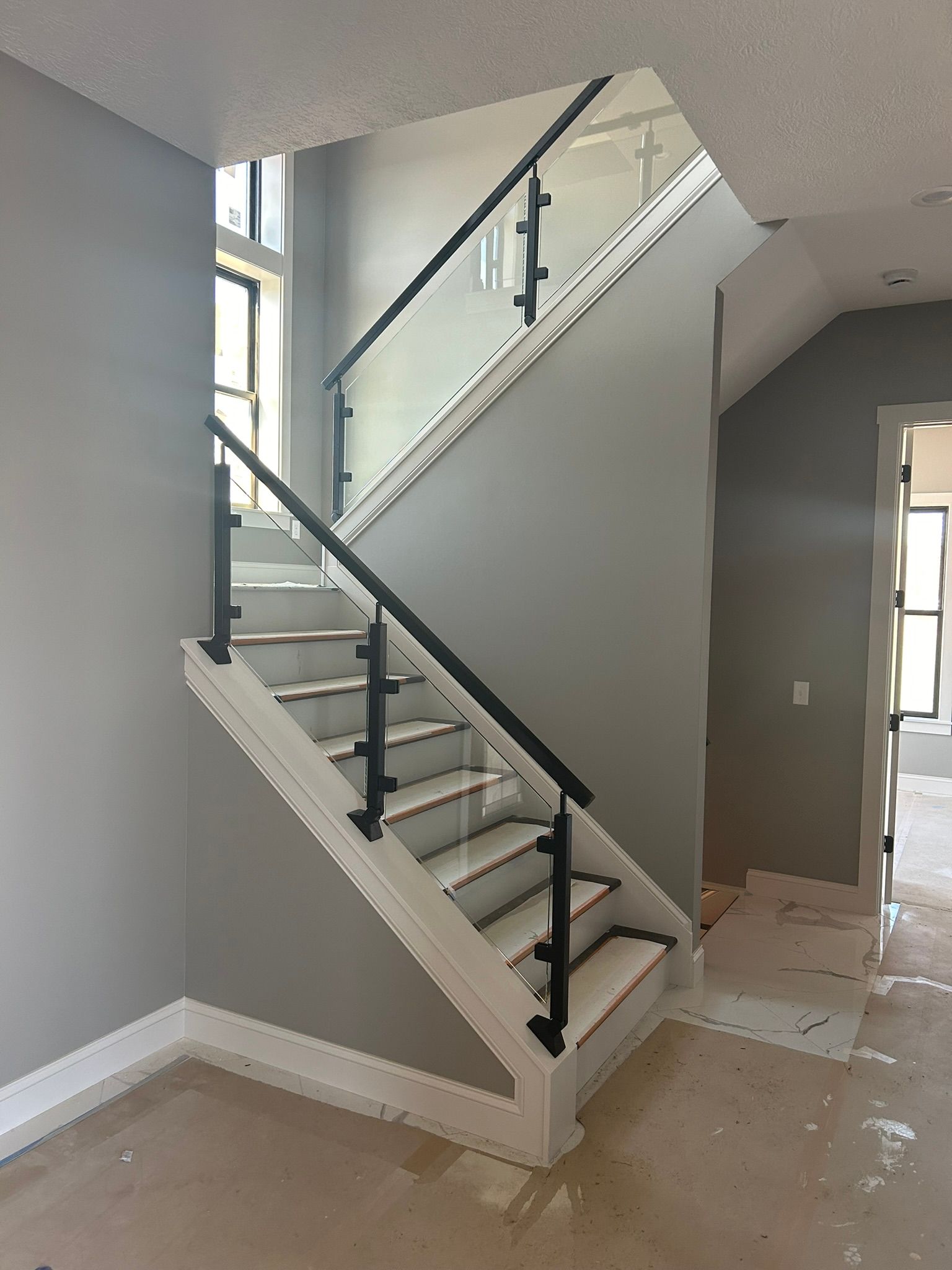 Staircase with glass and black metal railing, white trim, and gray walls.