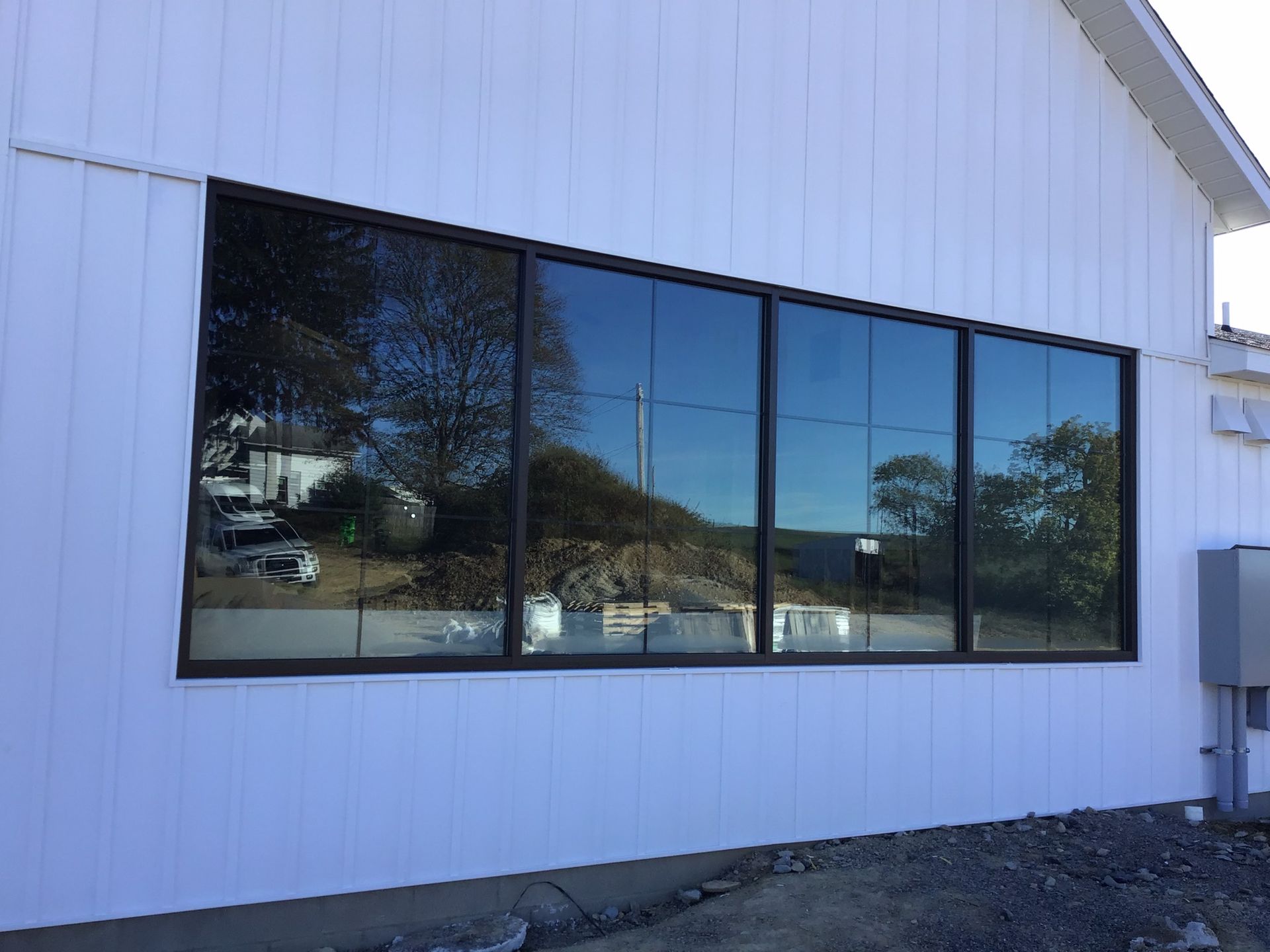 Large rectangular window with dark frames on a white building, reflecting trees and sky.