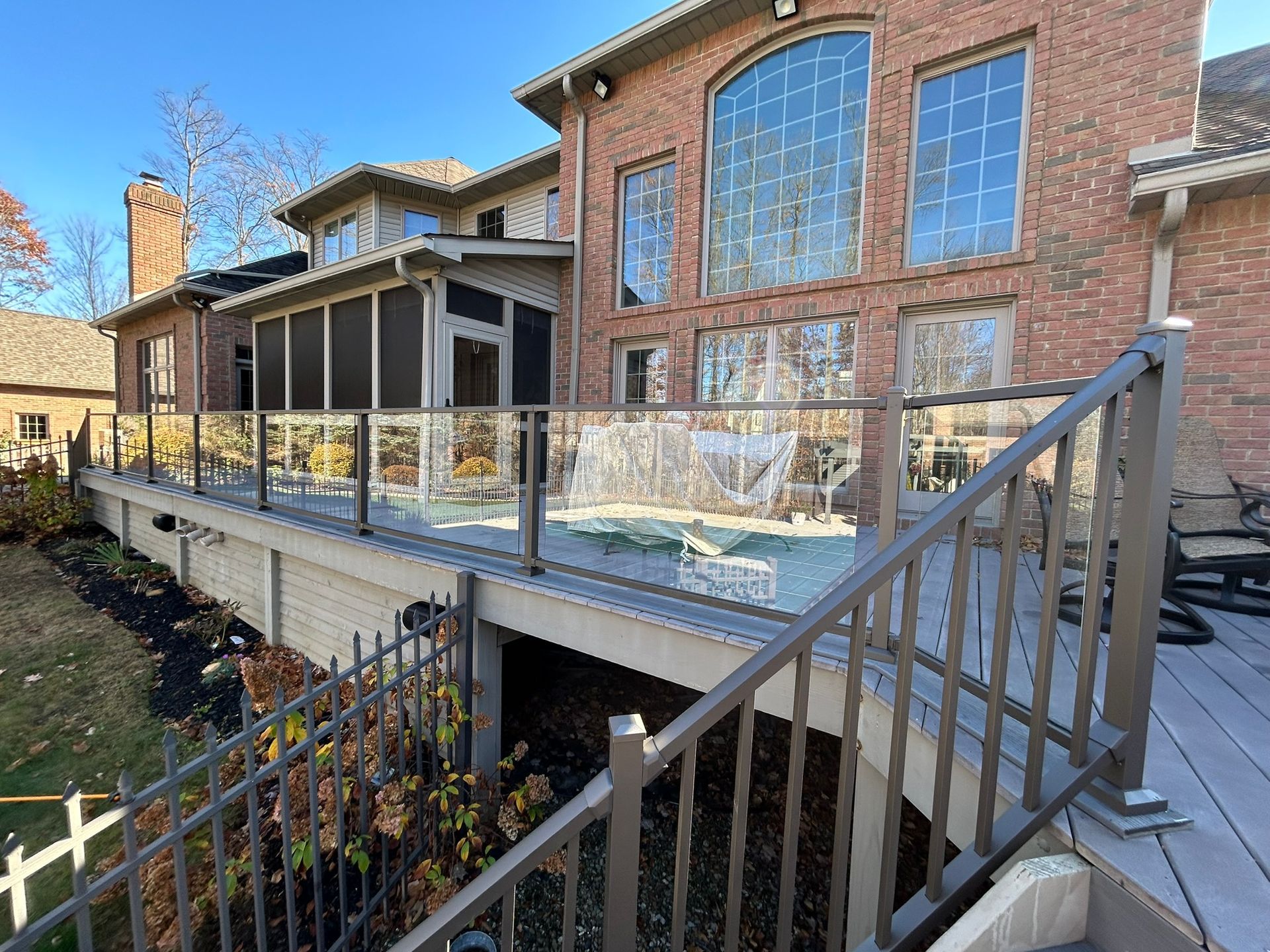 Backyard deck with glass railing, stairs, and brick house.