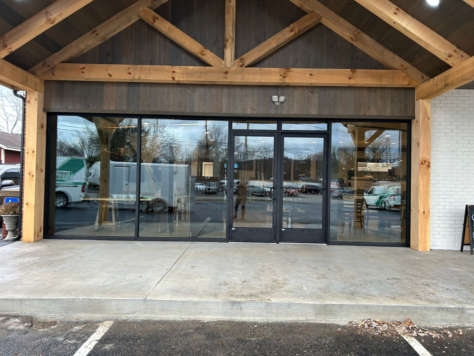 Storefront with large glass windows and wooden beams. Gray concrete sidewalk.