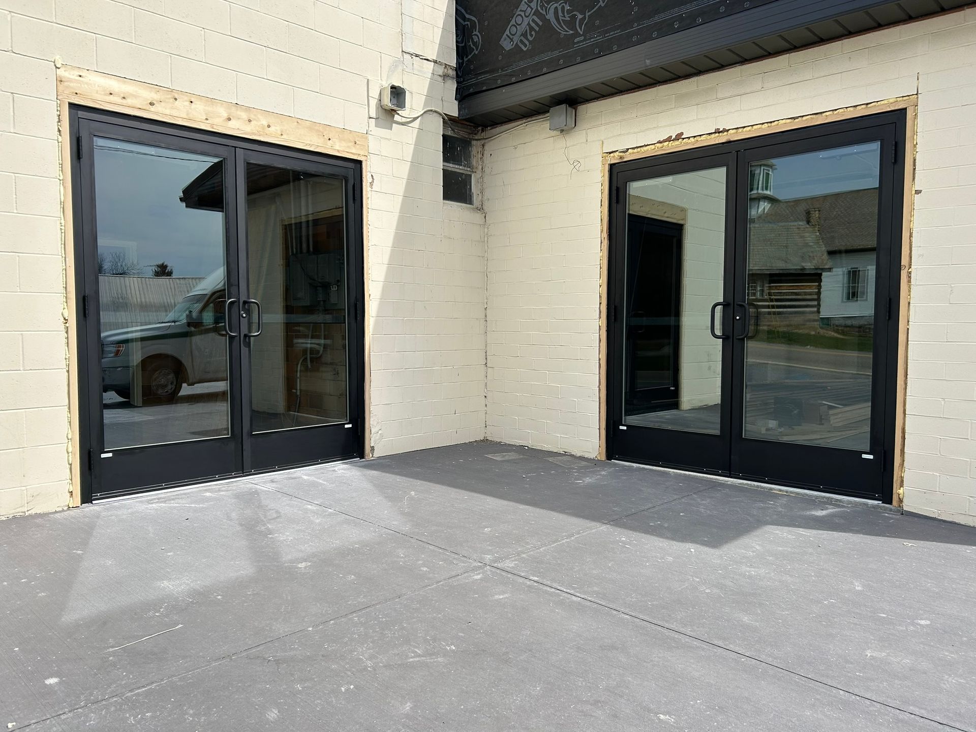 Two black-framed glass doors on a light gray patio, set in a light beige building exterior.