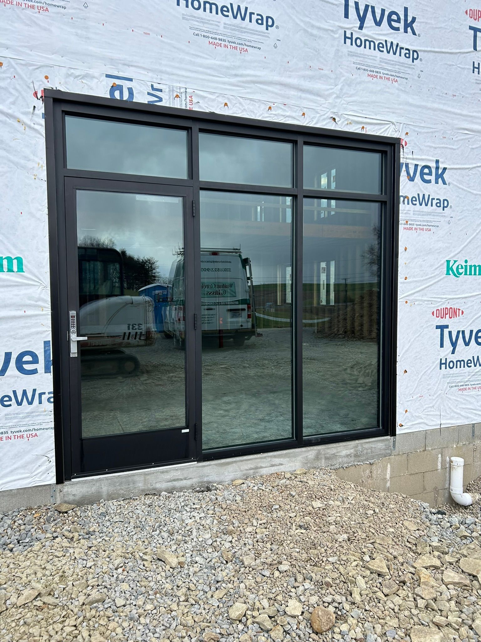 Black-framed door and window unit on a building under construction, reflecting construction equipment.
