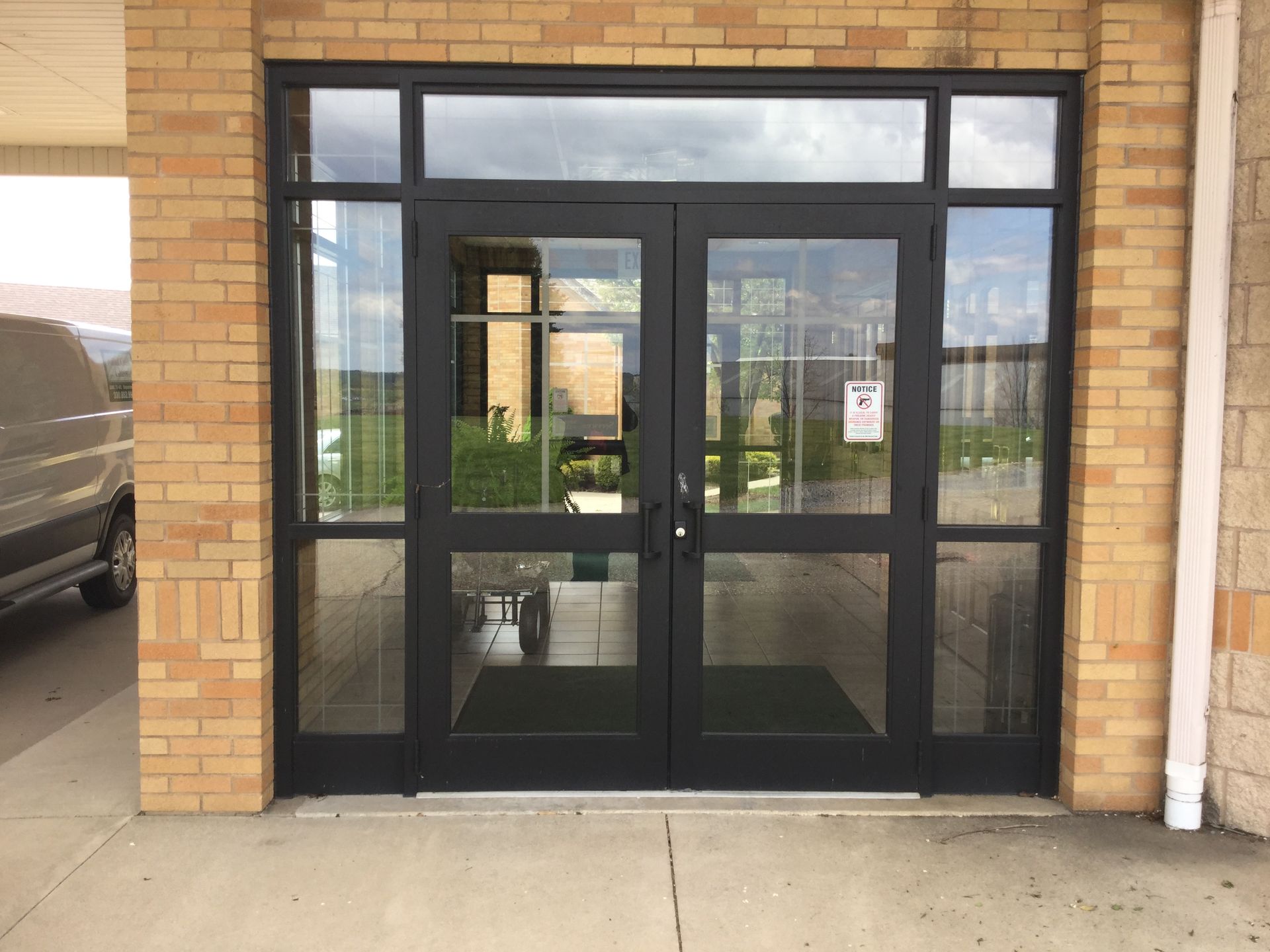 Black double doors with glass panels and a transom window on a brick building's entrance.