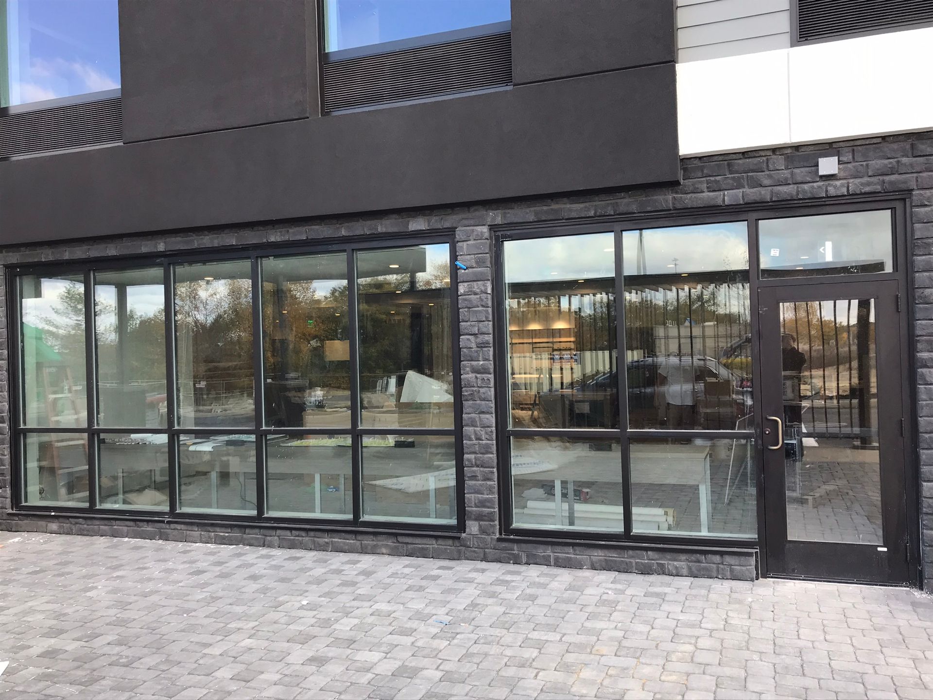 Storefront with large windows and a door, grey brick facade, and a paved walkway.