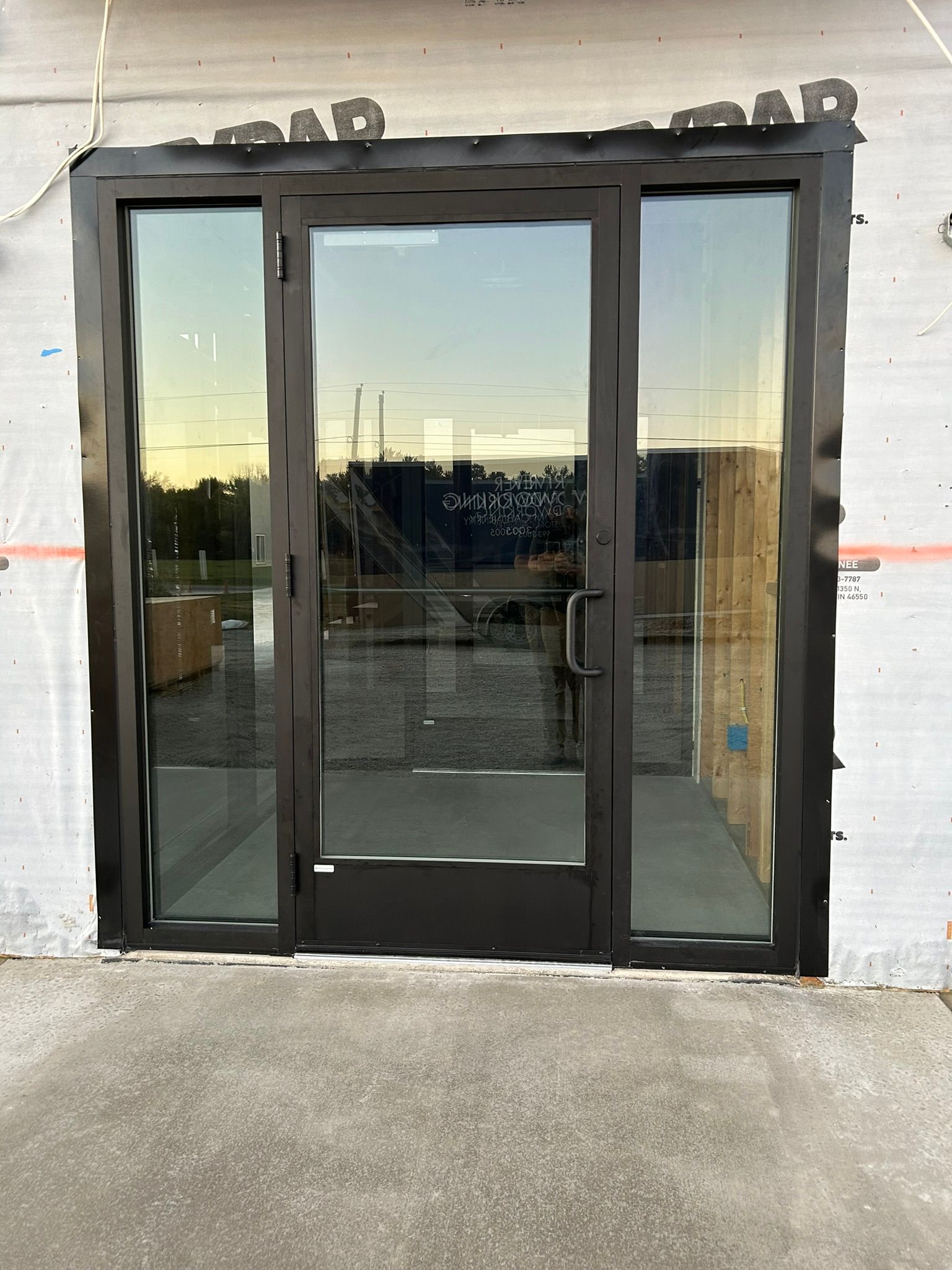 Black glass storefront door with sidelights. Building under construction.