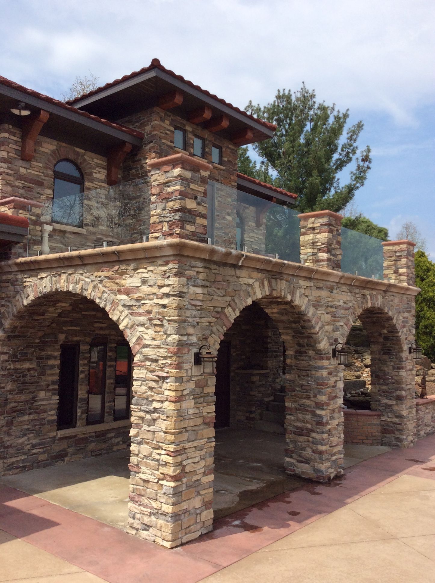 Stone building with arched columns and a balcony with glass railings.