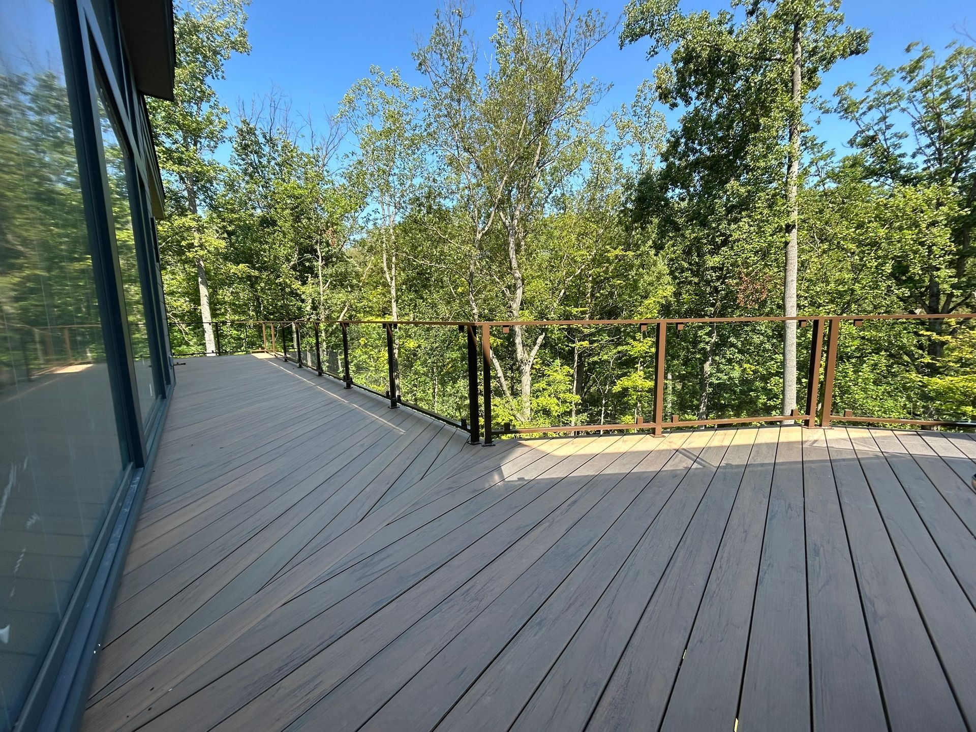 Deck with composite boards, metal railing, and surrounding trees under a blue sky.