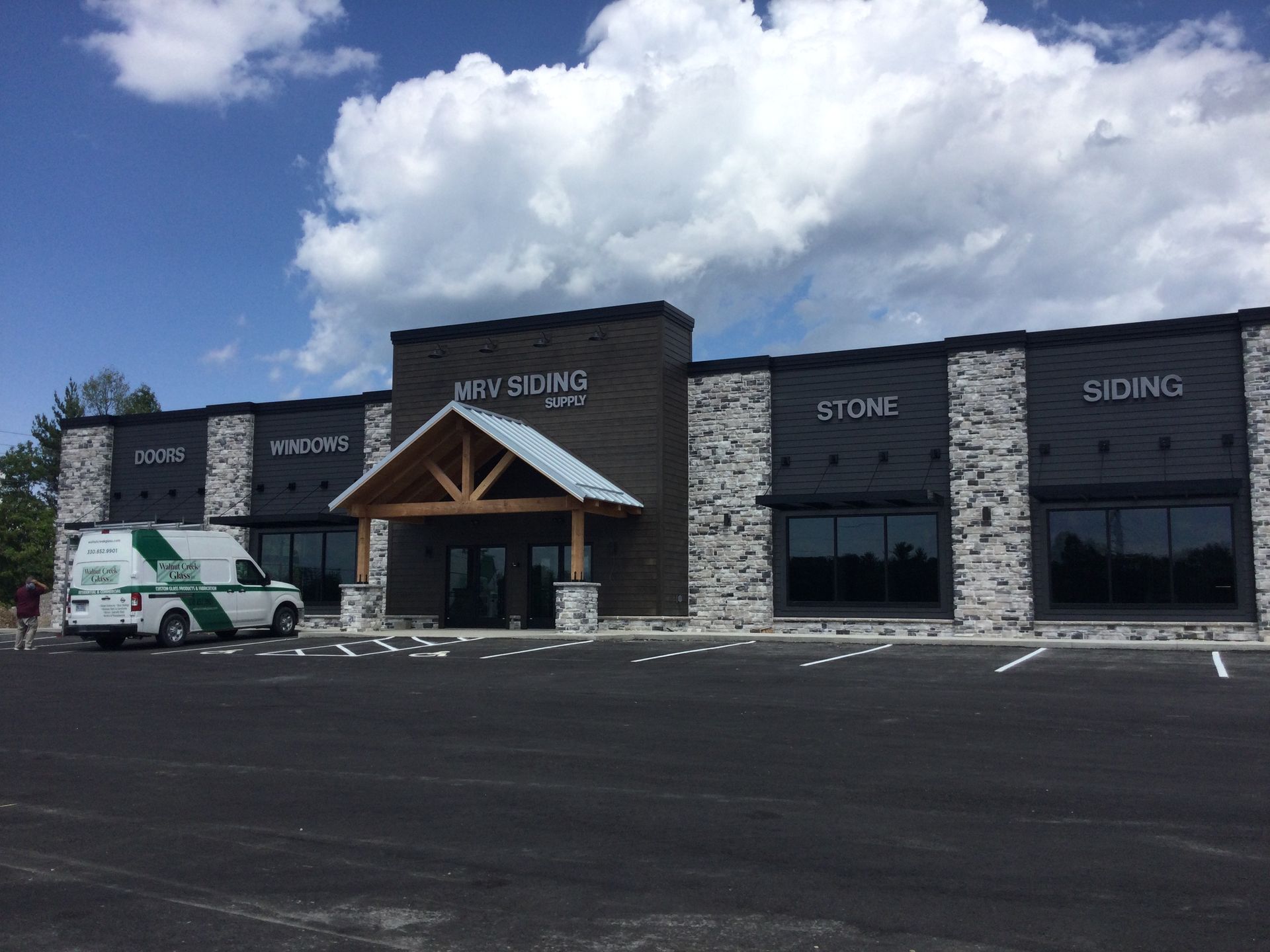 Exterior view of a commercial building. Features wood, stone and siding materials. A work van is parked in front.
