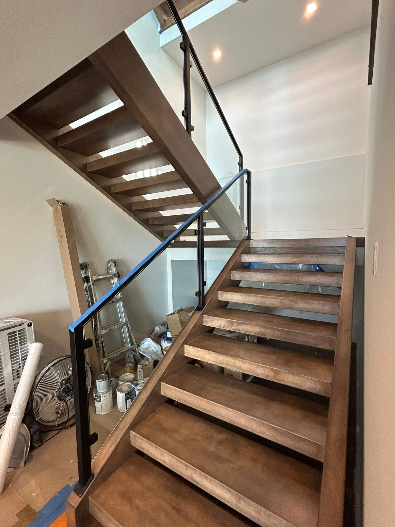 Wooden staircase with glass and black metal railing, leading to an upper level.