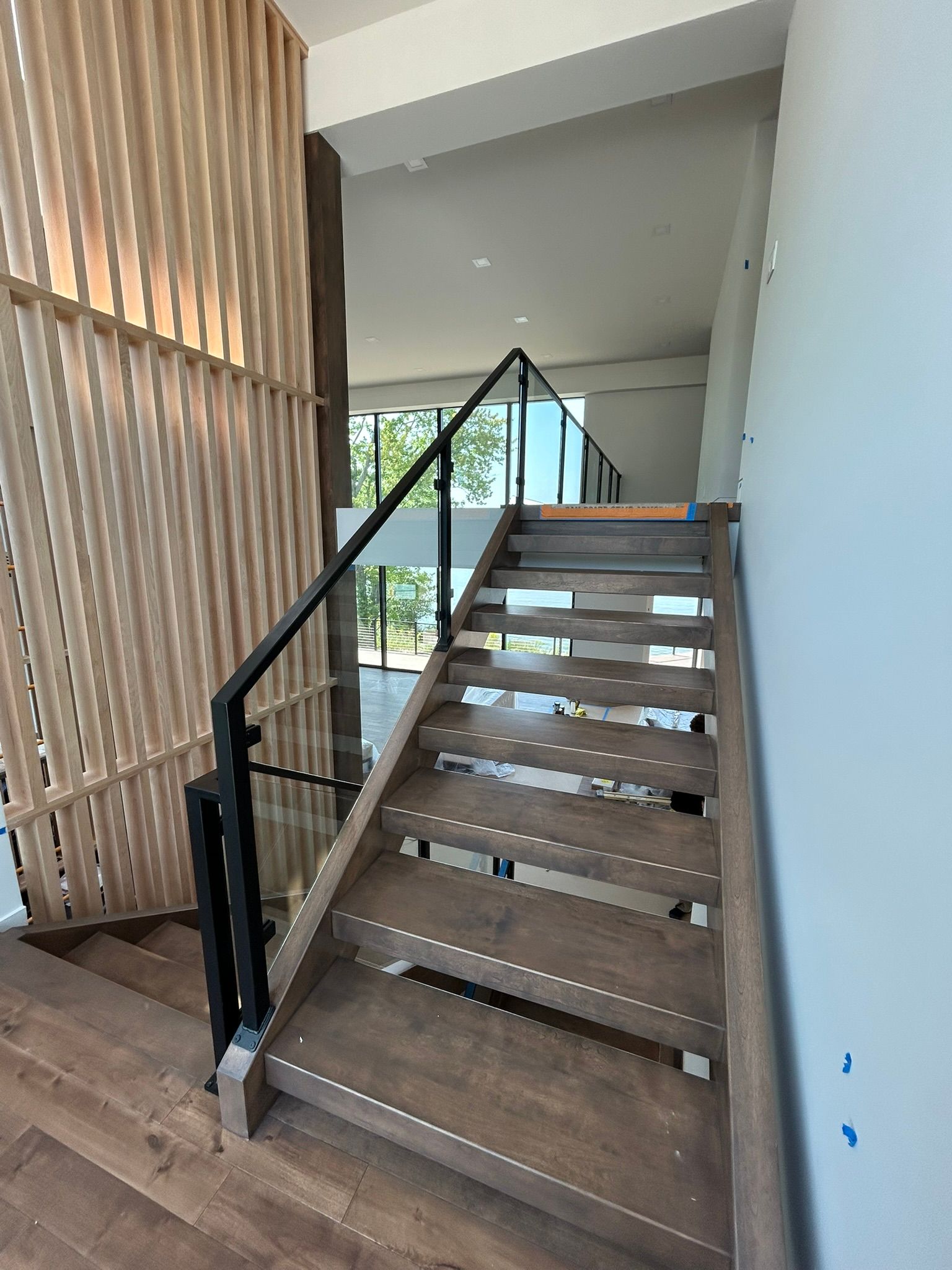 Wooden staircase with black handrails and glass panels. Vertical wooden slats on the left.