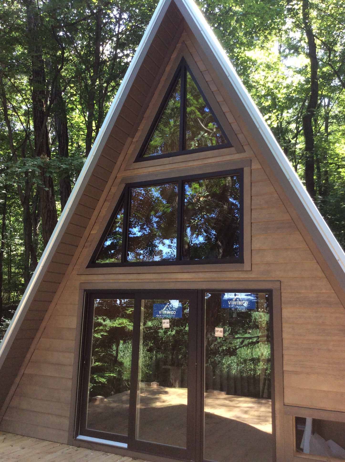 A-frame cabin with large windows reflecting trees, set in a forest.