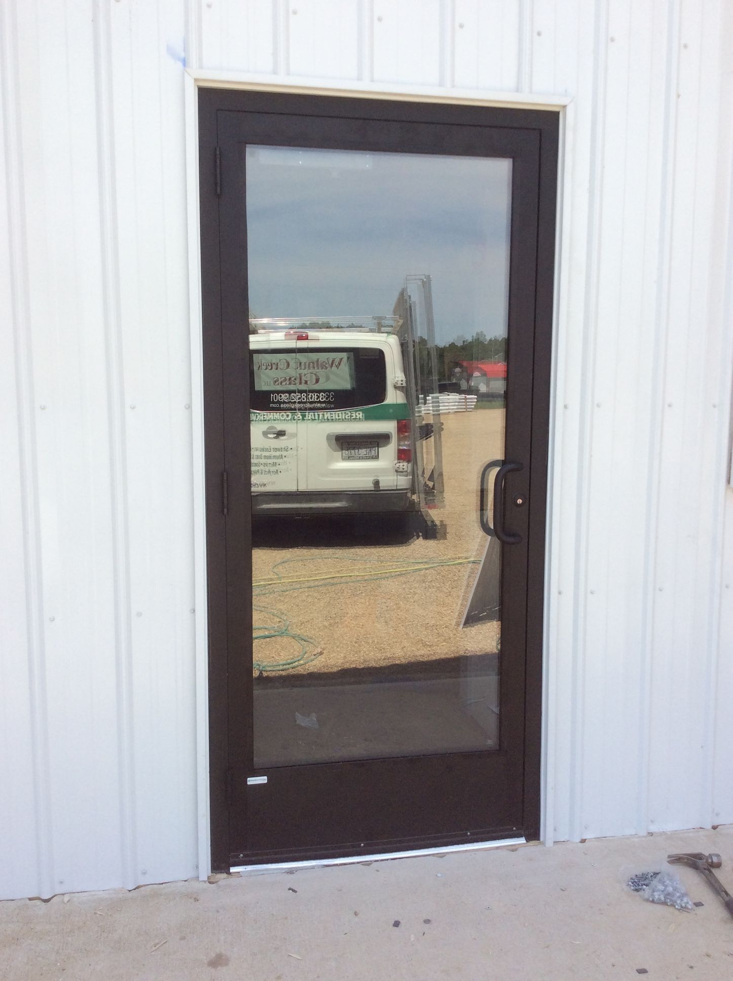 Glass door in a brown metal frame. Reflects a white van with green accents and surrounding environment.