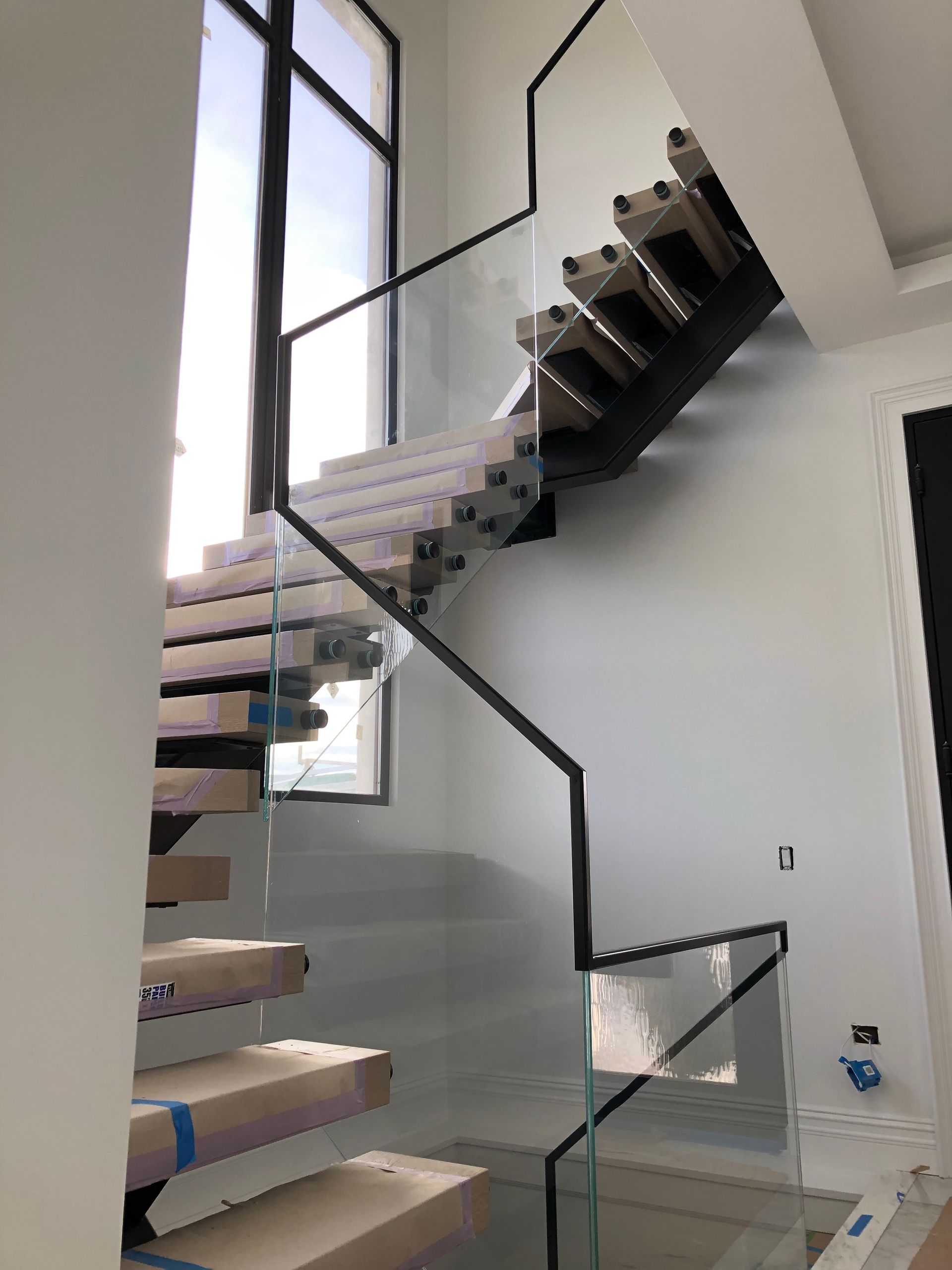 Modern staircase with wooden treads, glass panels, and black metal handrails.