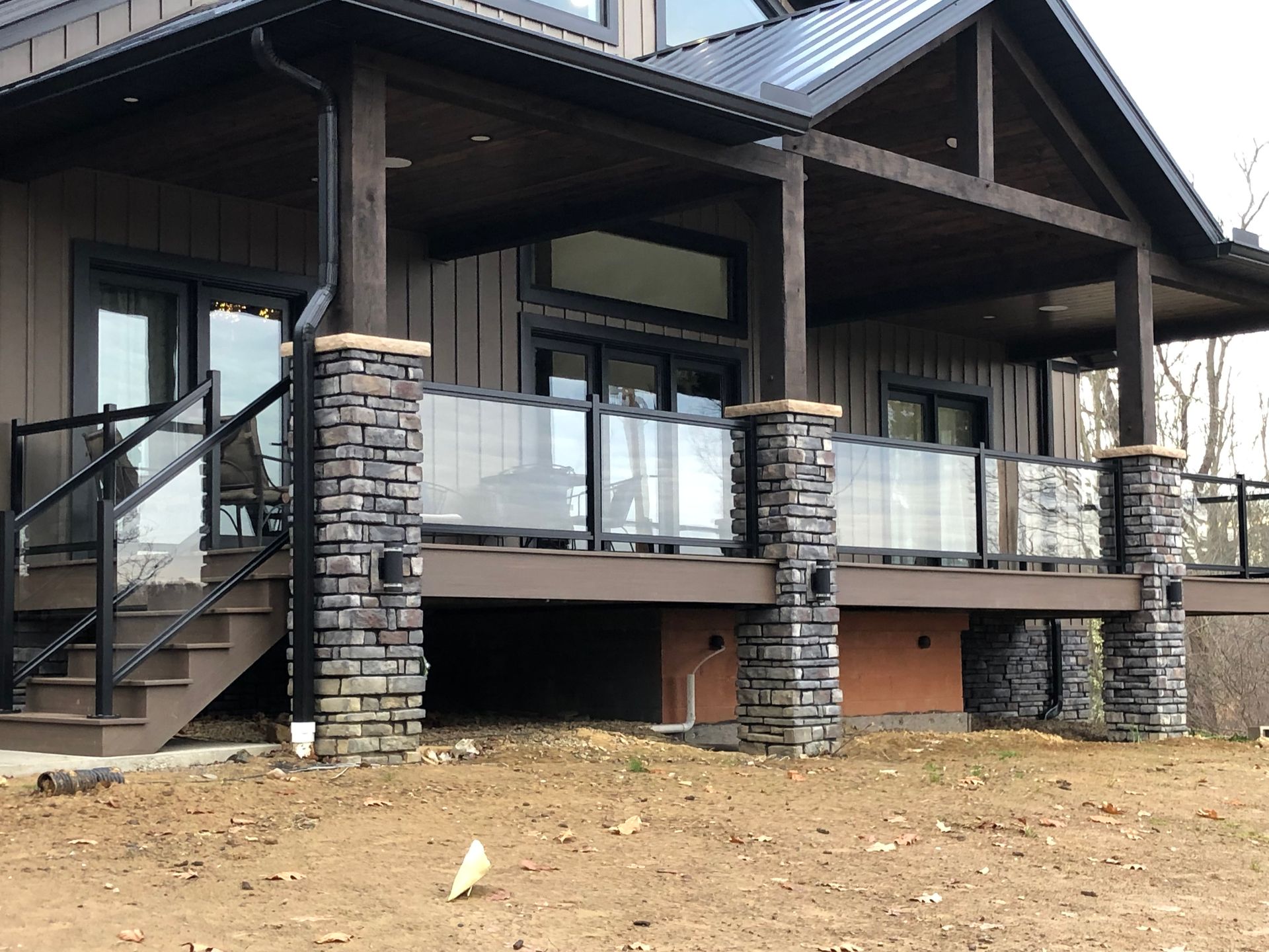 Brown house with a covered porch featuring glass and stone railings, and stairs.