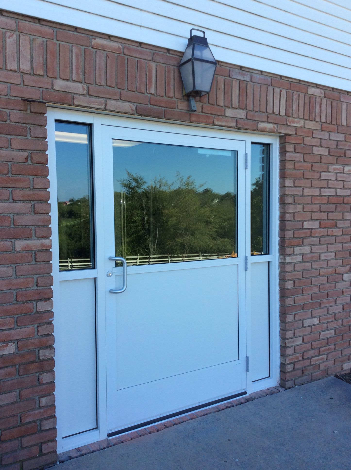 White door with window and sidelights, set in brick wall with a lantern above.