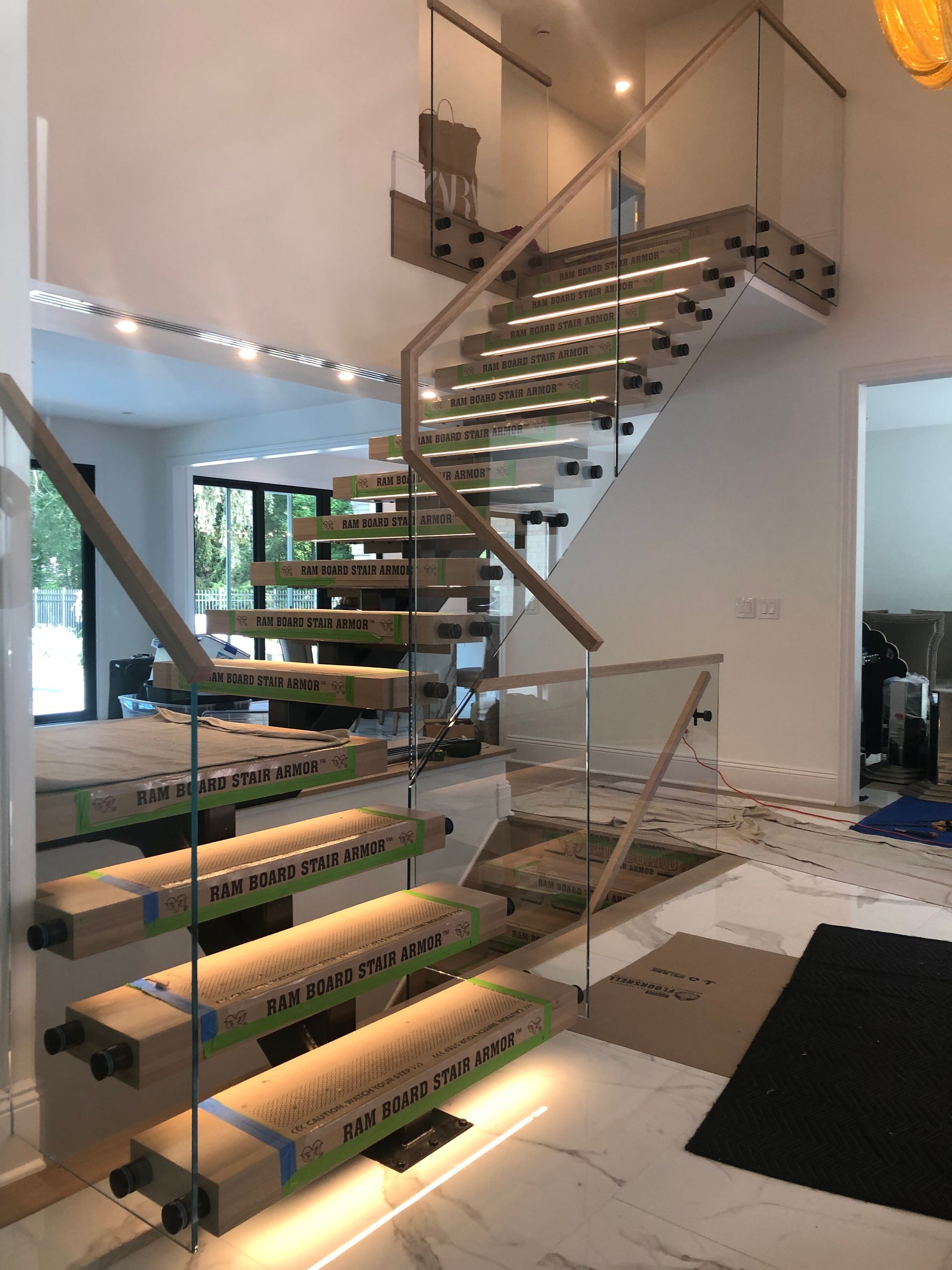 Modern staircase with wooden steps, glass railings, and under-step lighting, in a home interior.