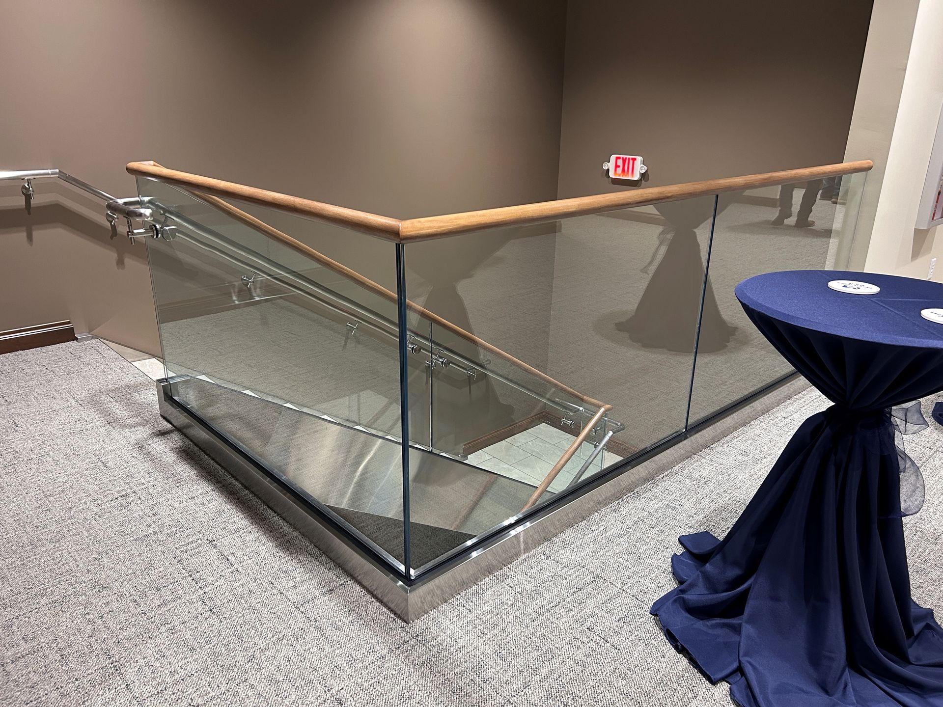Staircase with glass panels and wooden handrail; a blue-covered table is on the right.