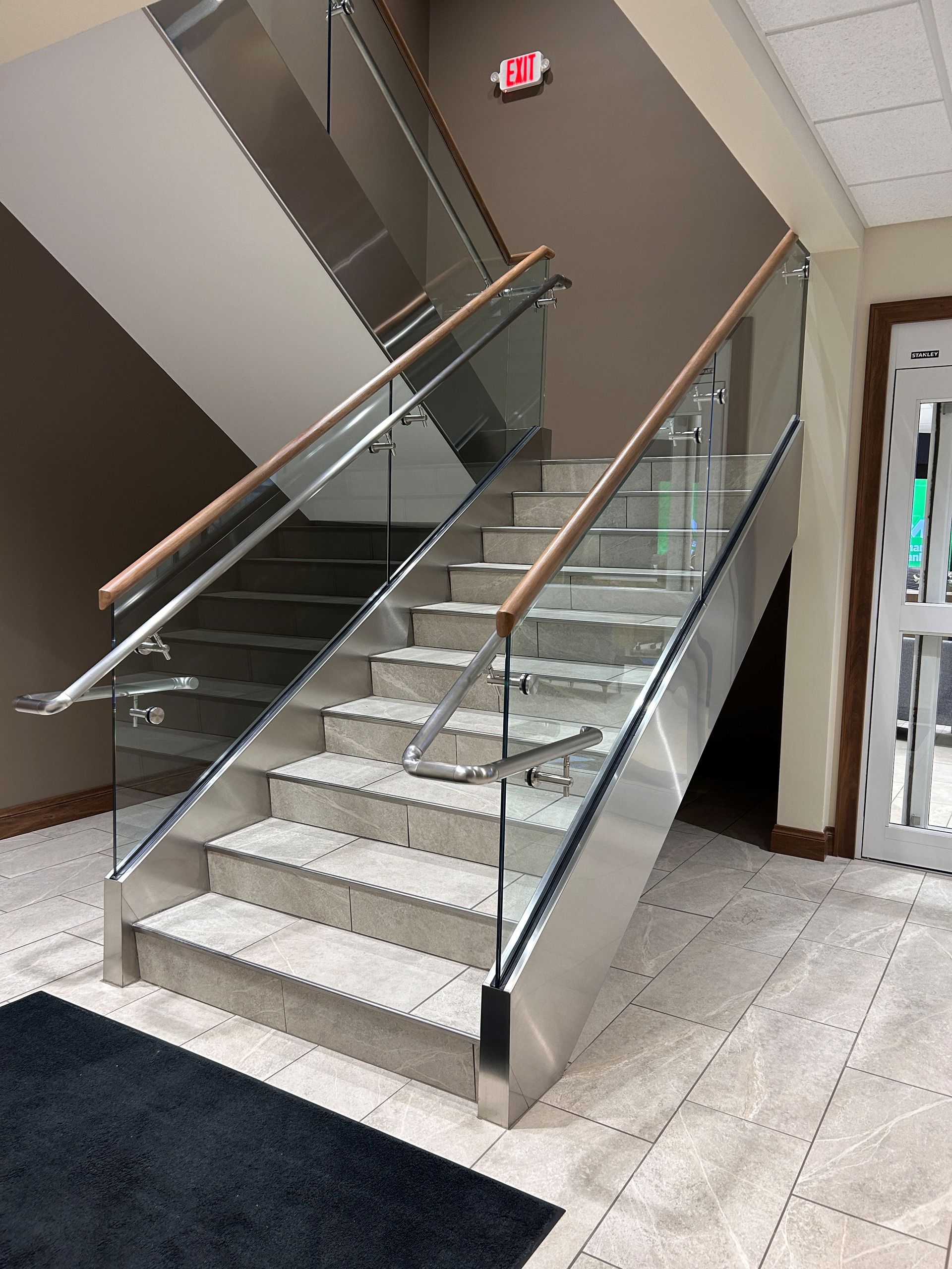 Staircase with glass and metal railings, wooden handrails, and tiled steps.
