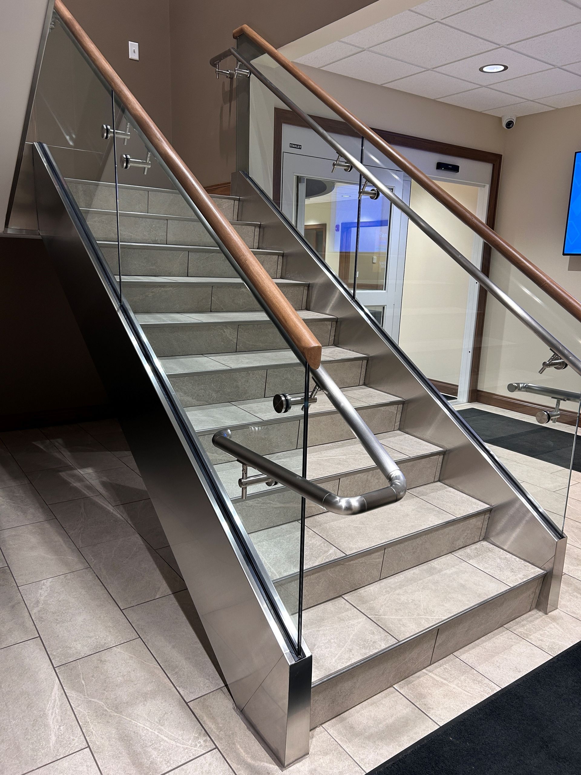 Staircase with stainless steel frame, glass panels, wooden handrails, and carpeted steps.