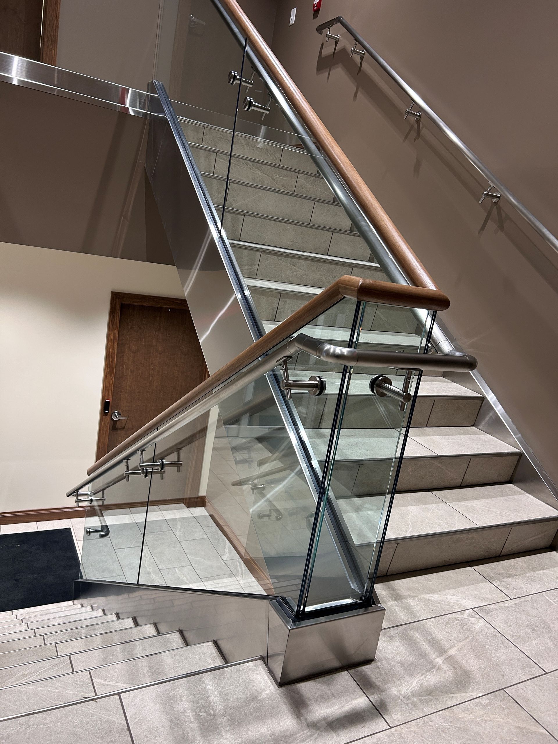 Staircase with glass and metal railings, and wooden handrail. Marble steps lead upward.