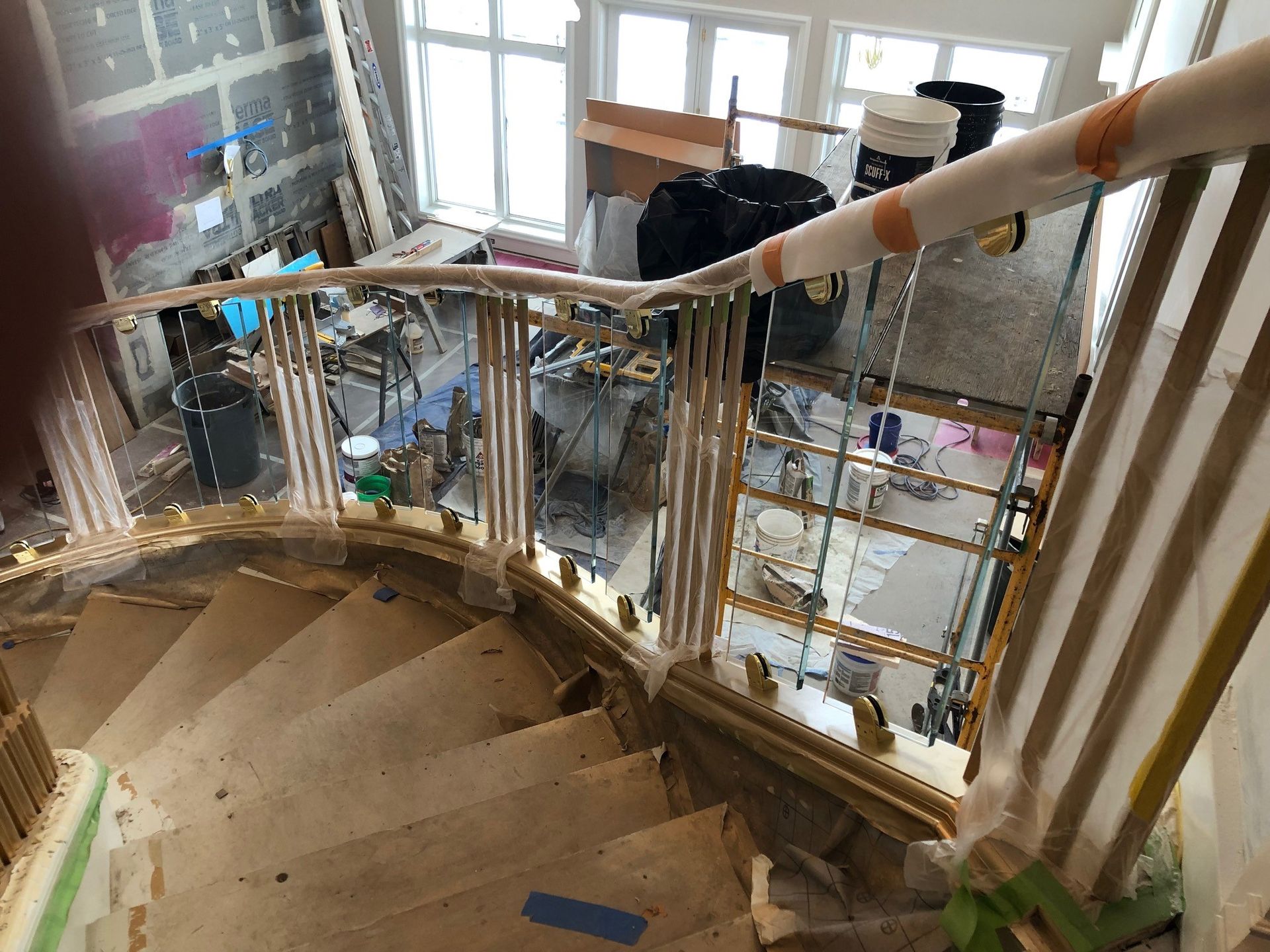 Staircase with glass and metal railing under construction, leading to a room with windows and equipment.