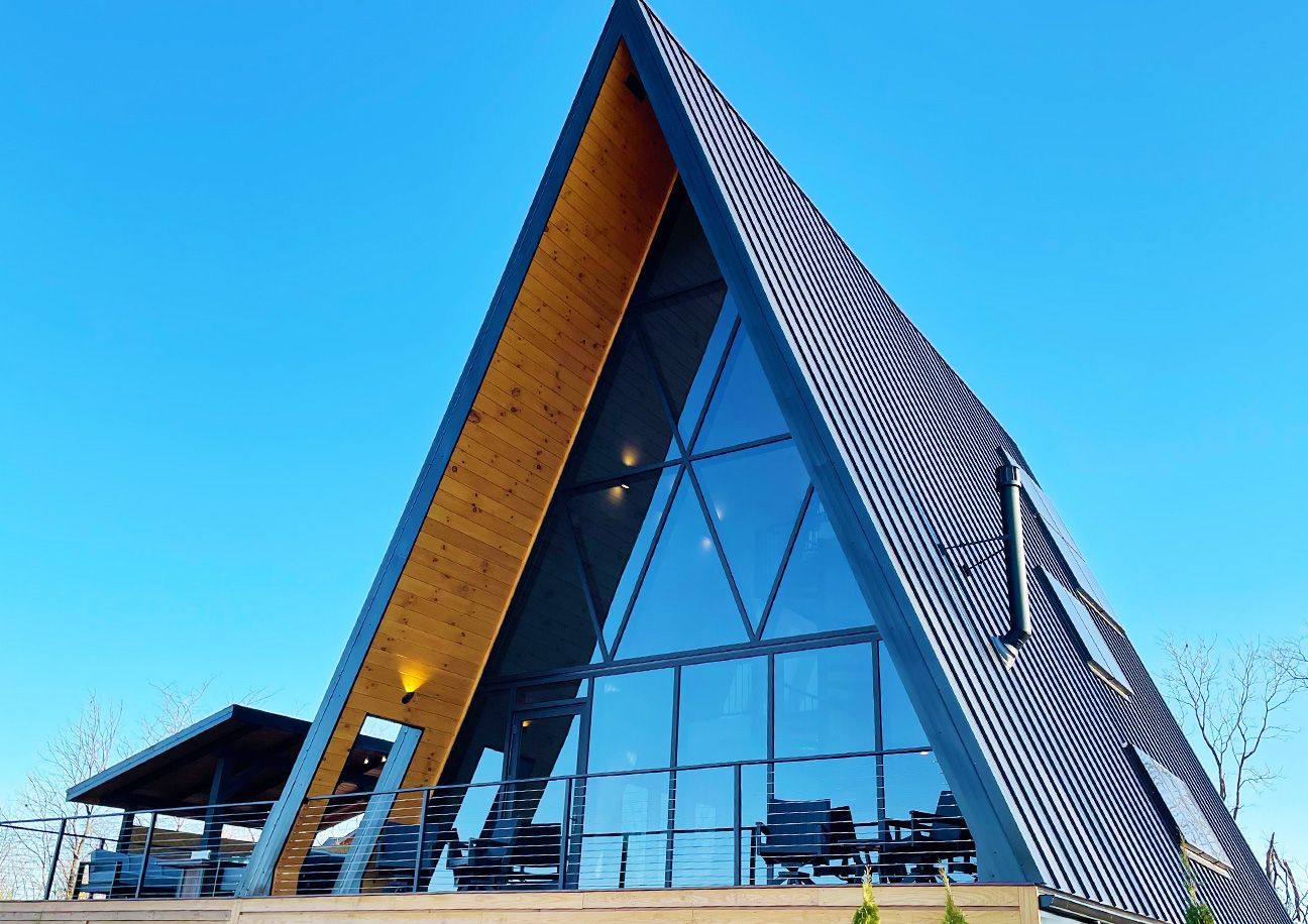 A black building with a triangle shaped roof is sitting on top of a grassy hill.