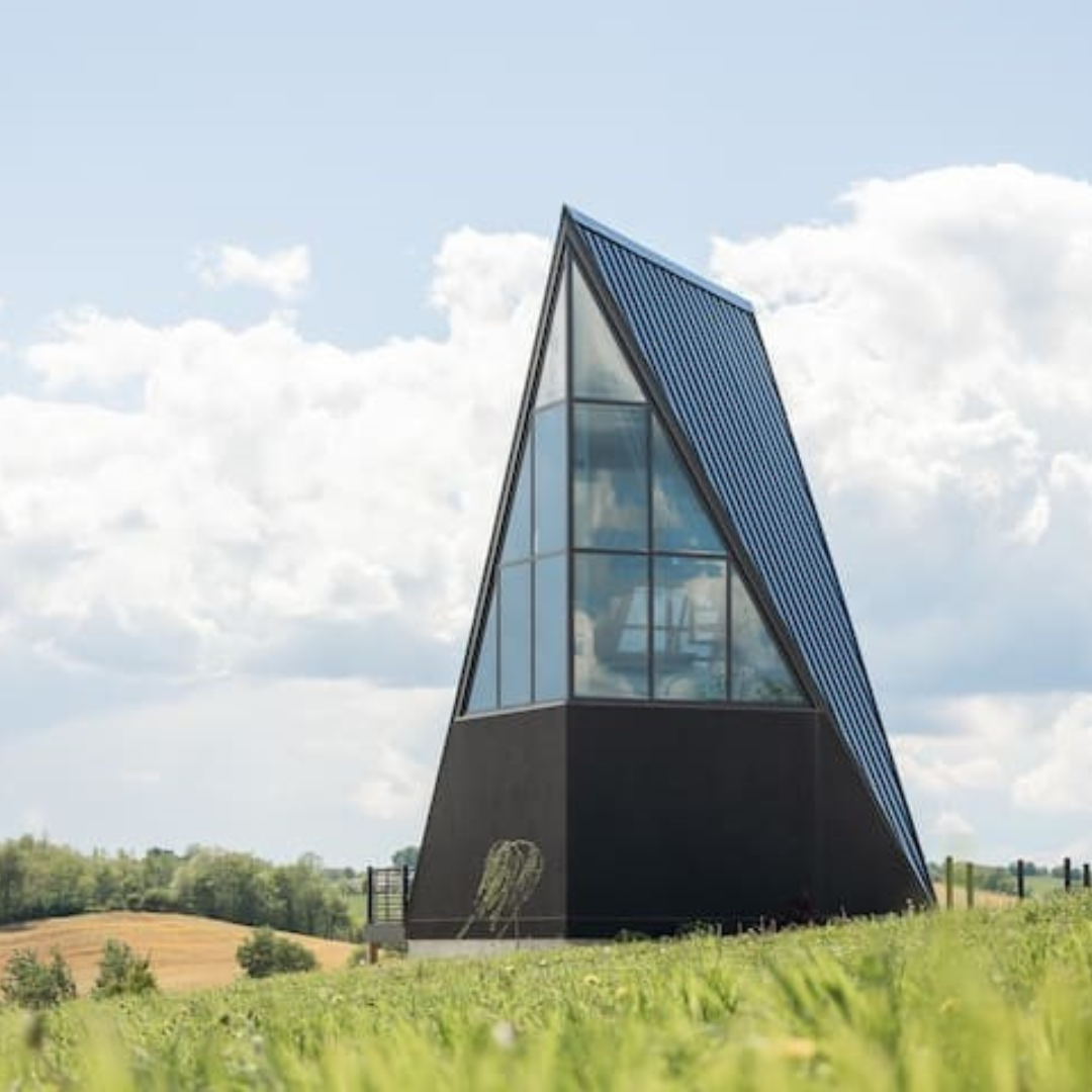 A black triangle shaped building is sitting on top of a grassy hill.