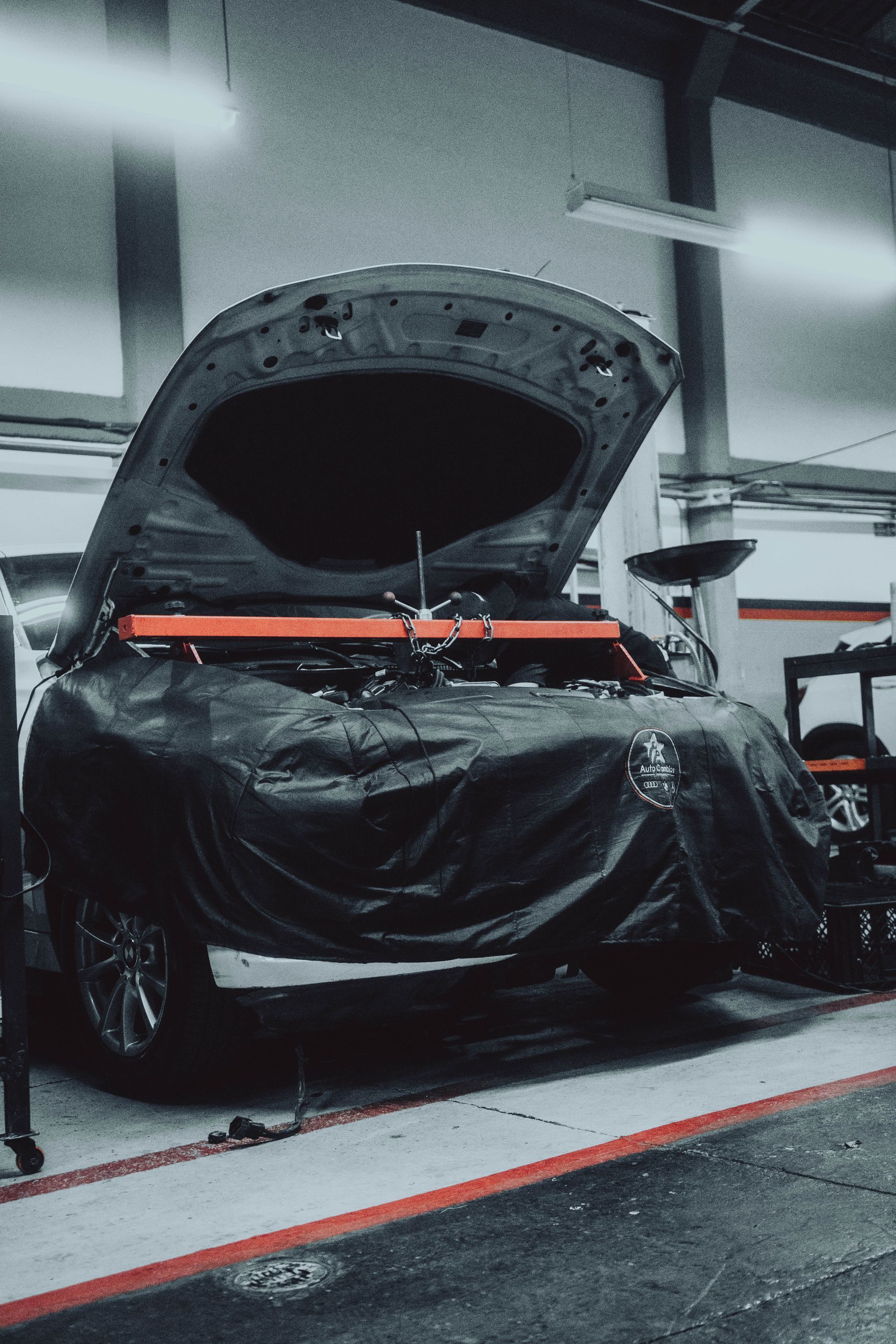 A car is being worked on in a garage with the hood open.