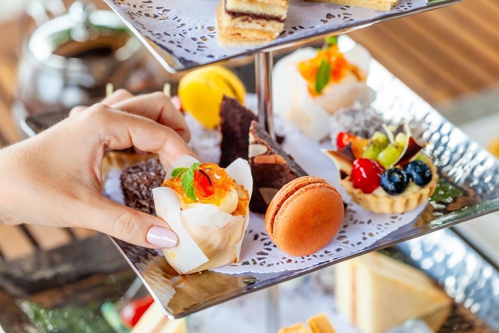 A person is holding a cupcake over a tray of desserts.