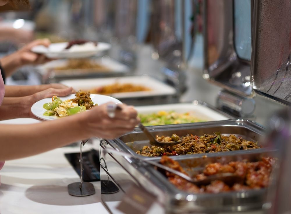 A person is taking a plate of food from a buffet line.