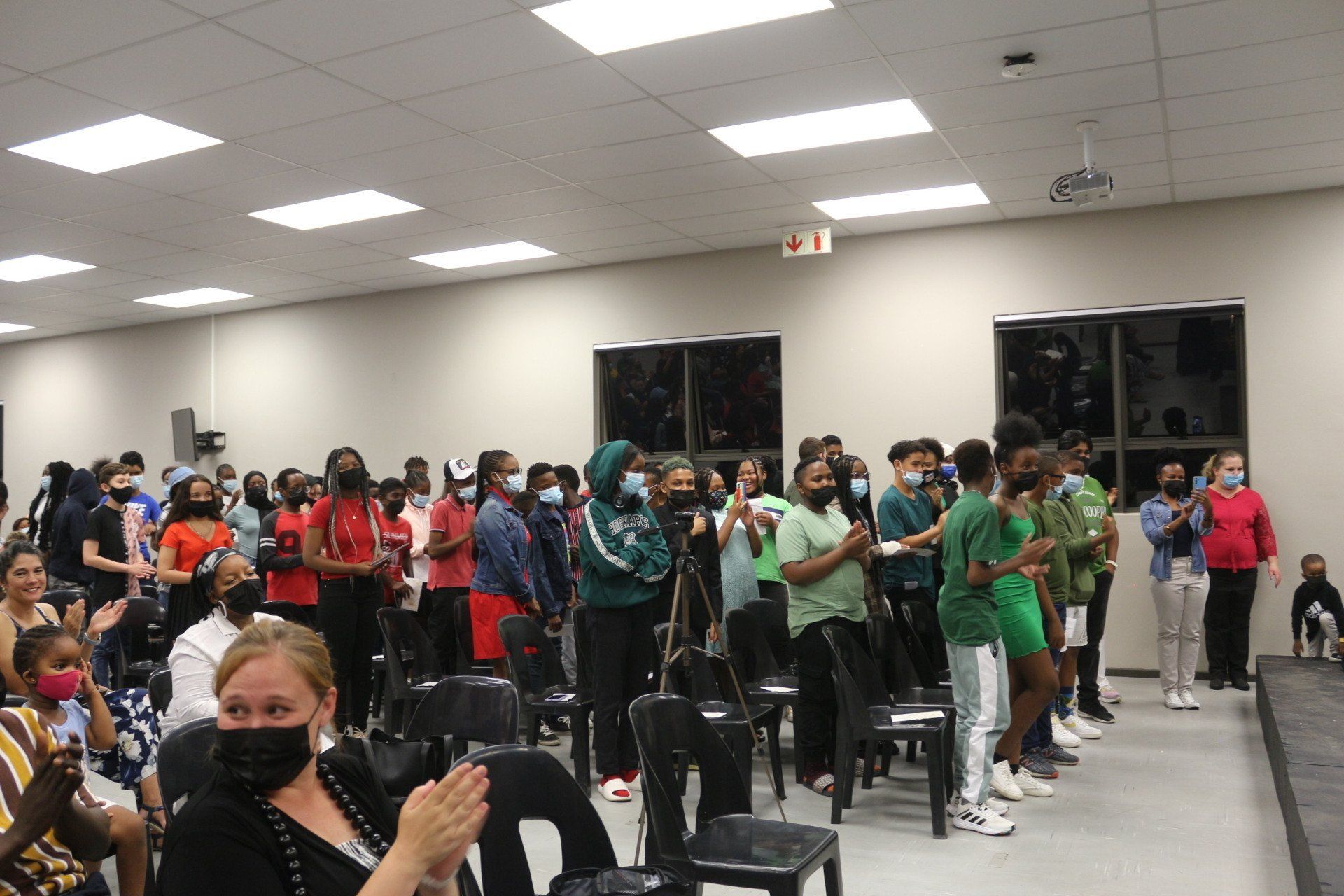 A large group of people are standing in a room applauding.