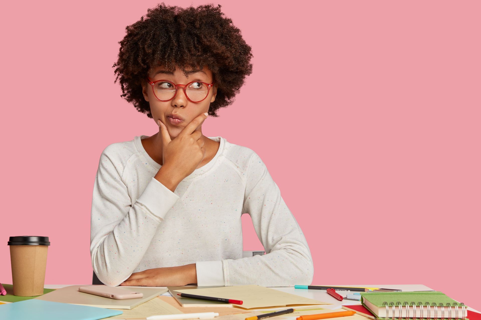 A young woman is sitting at a desk with her hand on her chin.